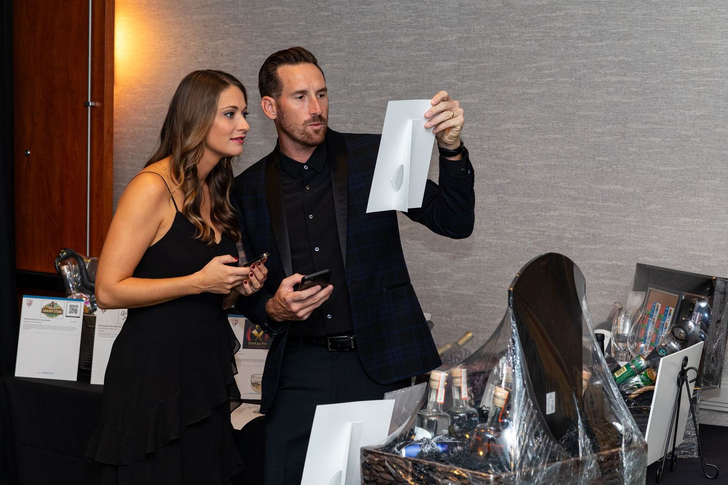 A man and woman in formal attire examine an envelope at an elegant charity auction event.