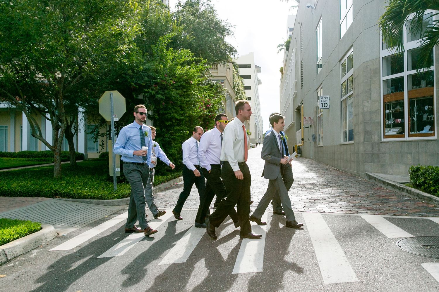 Four groomsmen in suits walking across a crosswalk on a sunny day.