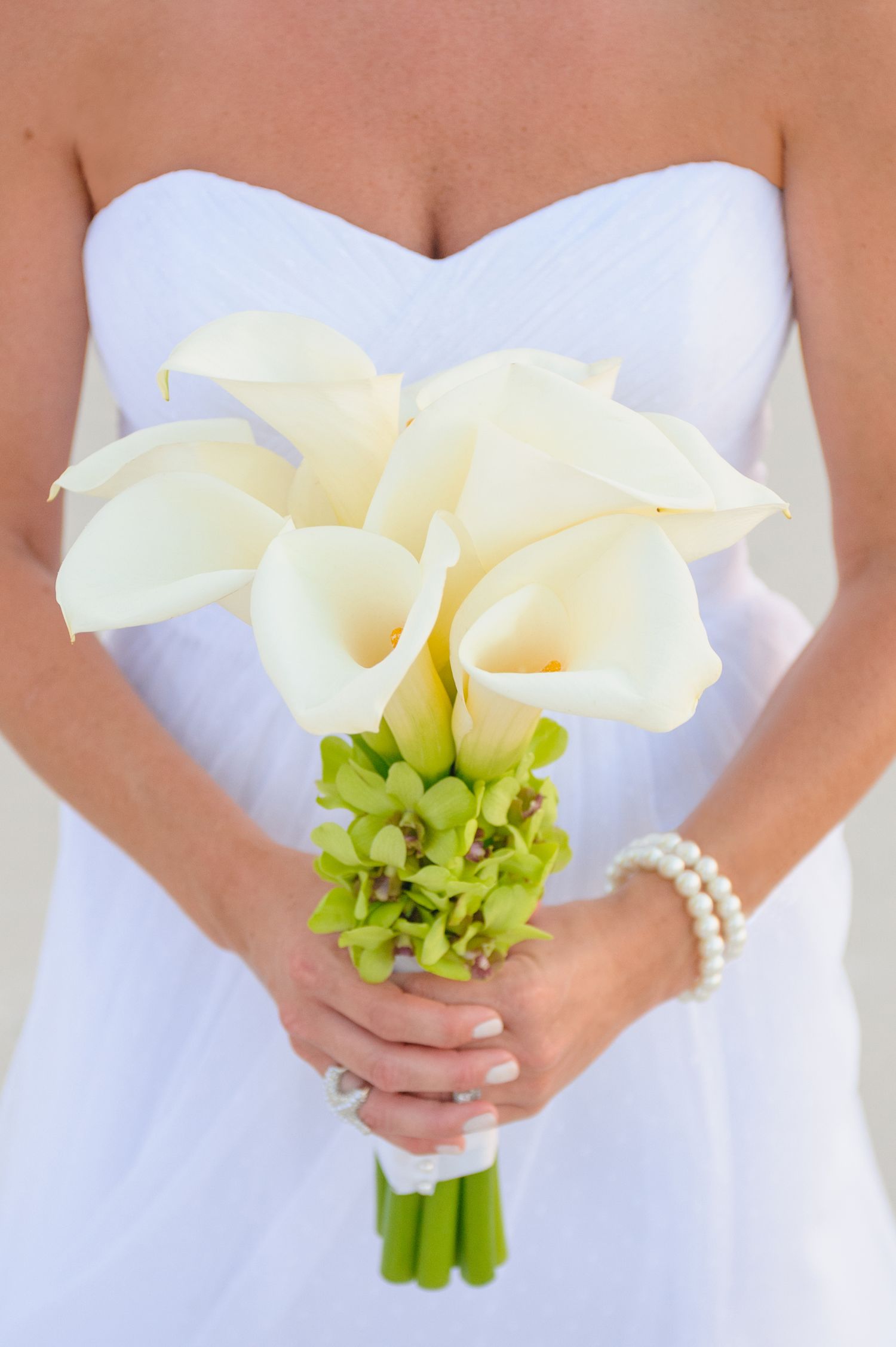 Bride holding a beautiful bouquet of white calla lilies with green accents on her wedding day.