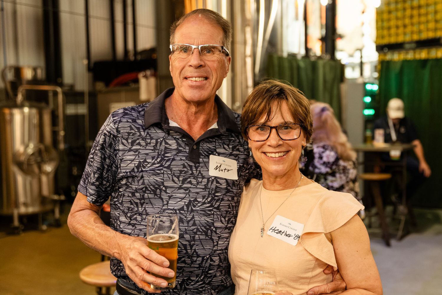 Smiling couple holding beers and wearing name tags at a brewery social event.