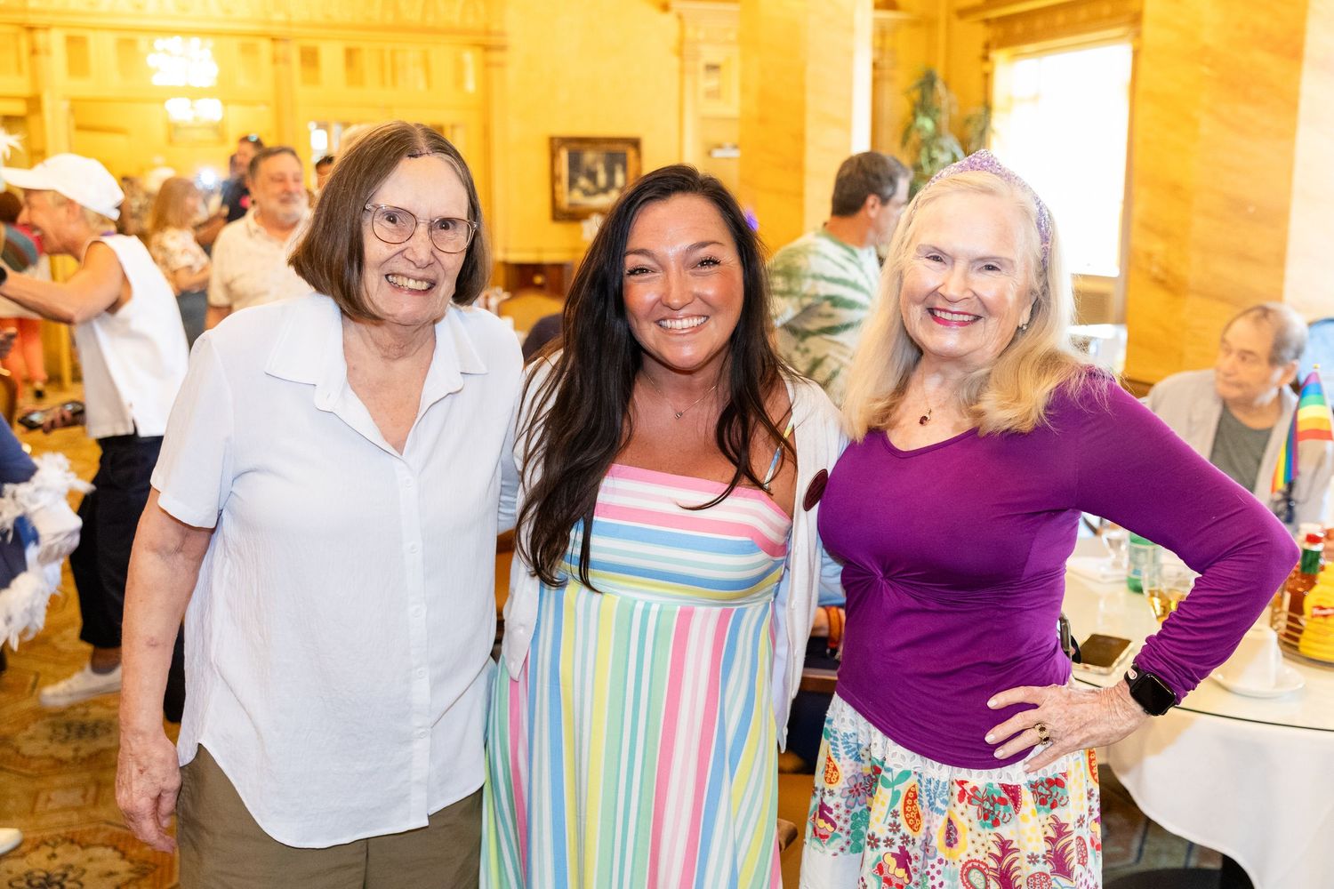 Three smiling women posing together at a casual indoor social gathering event.