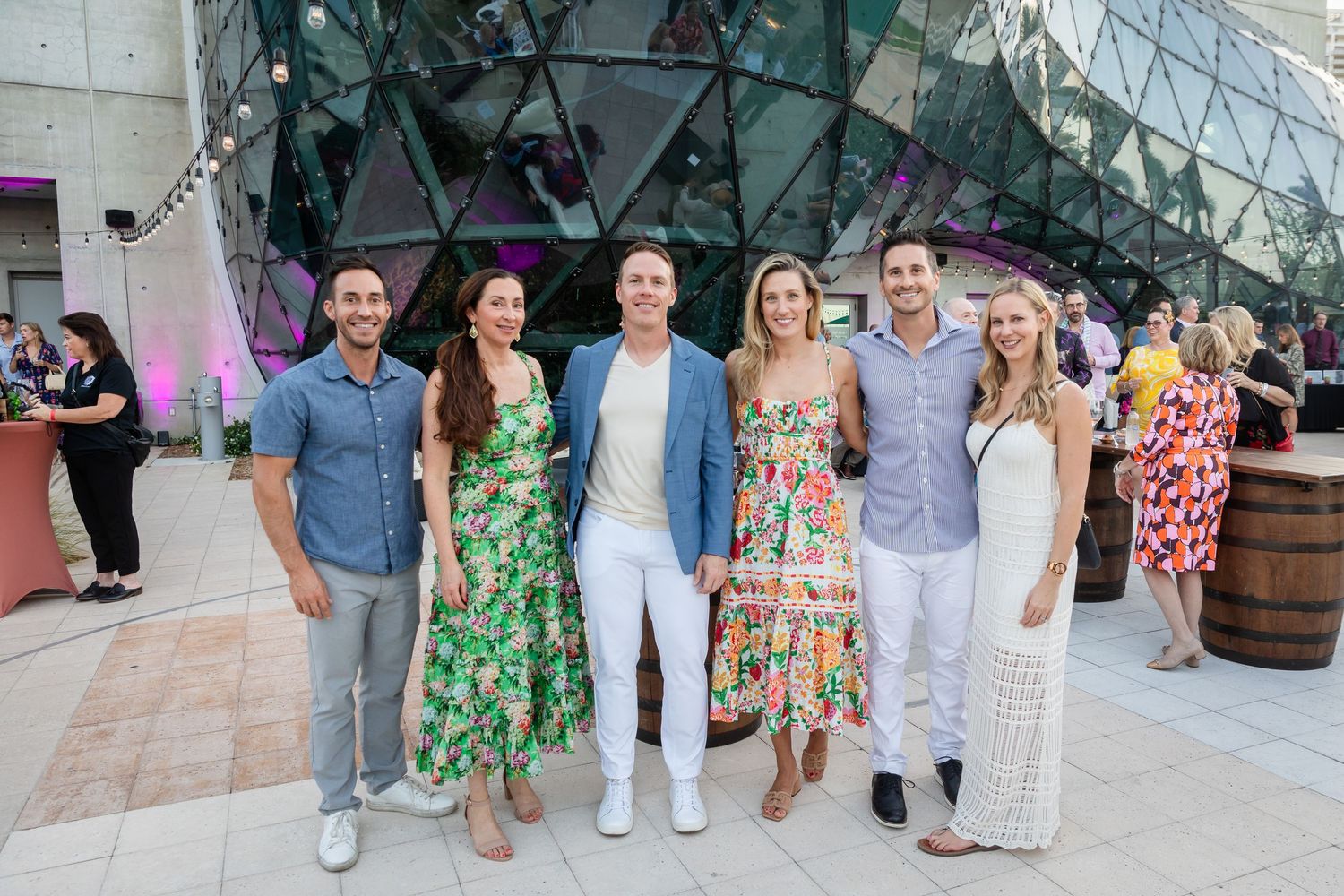 Six friends pose together outdoors at a summer evening event near a modern glass dome building.