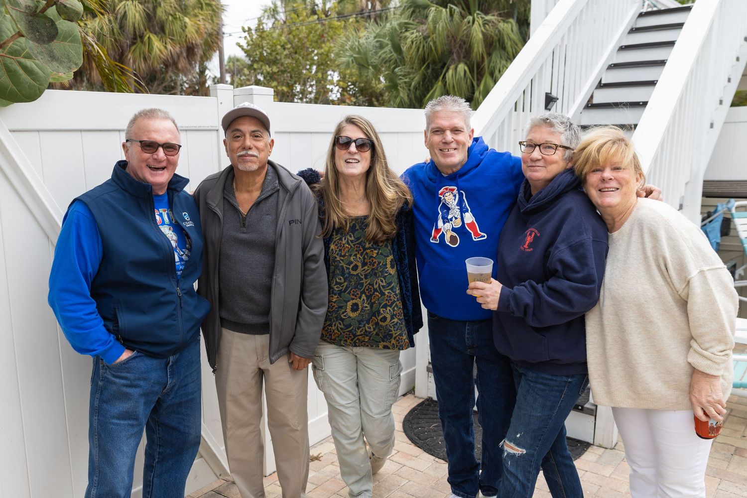 Six friends pose together outdoors near white stairs, smiling for a group photo on a cloudy day.
