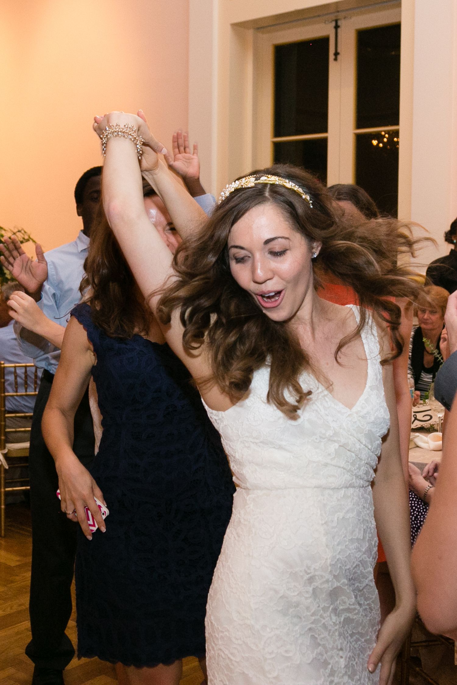 Bride in white lace dress dancing joyfully with guests at wedding reception.