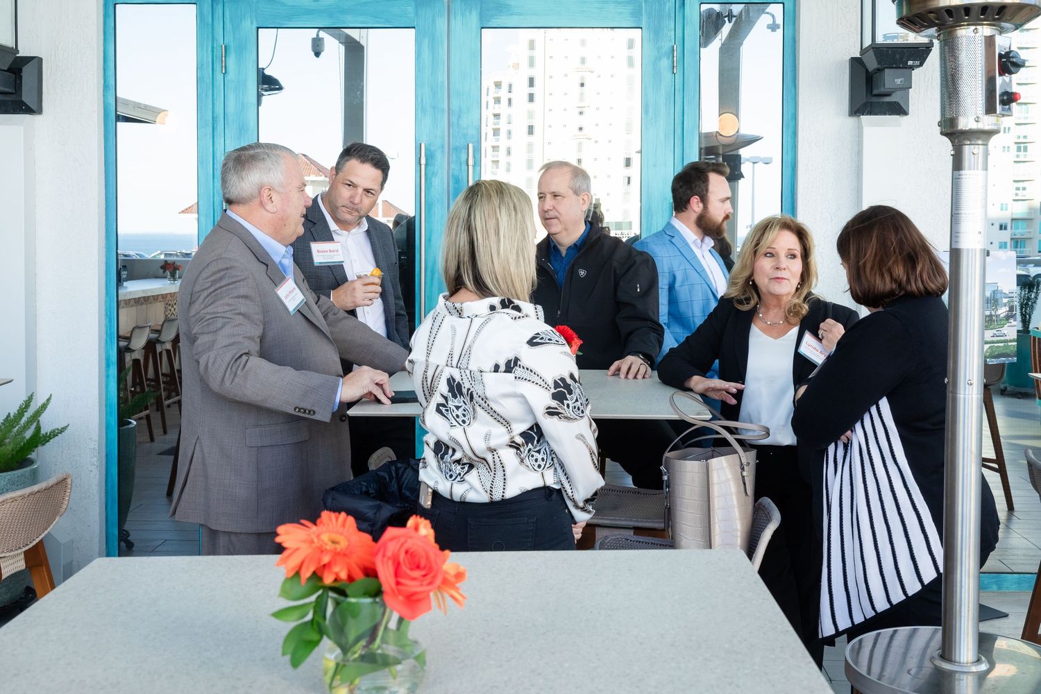 Professionals networking at an outdoor corporate event on a patio with teal accents and floral centerpieces.