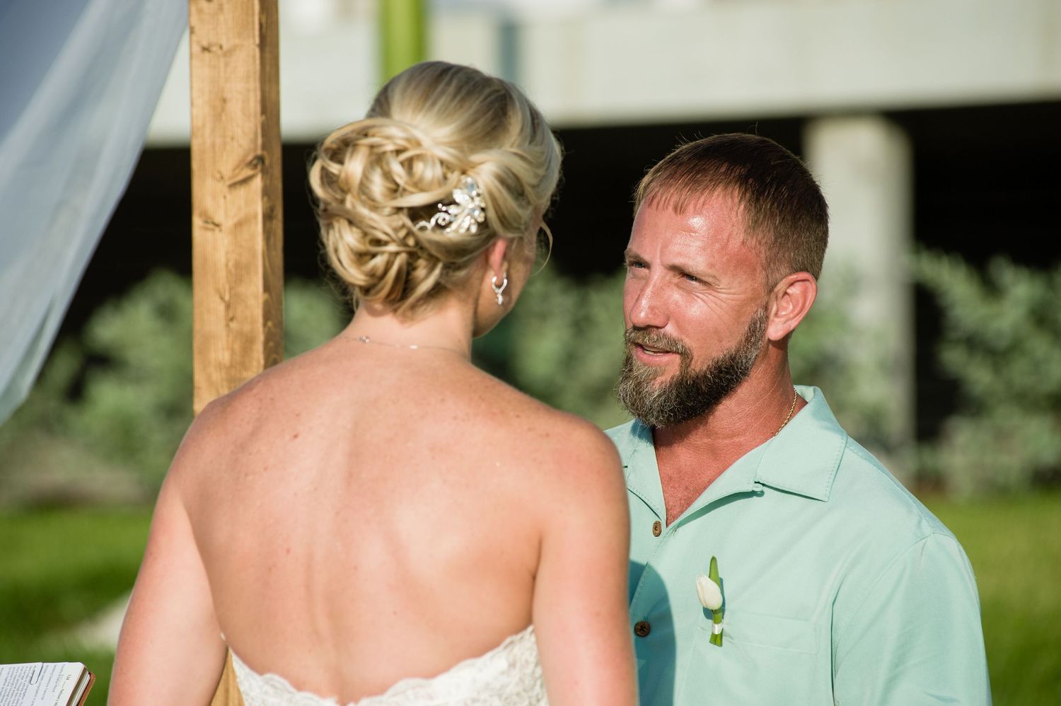 Bride and groom share a heartfelt moment during outdoor wedding ceremony, groom wearing mint green polo shirt.