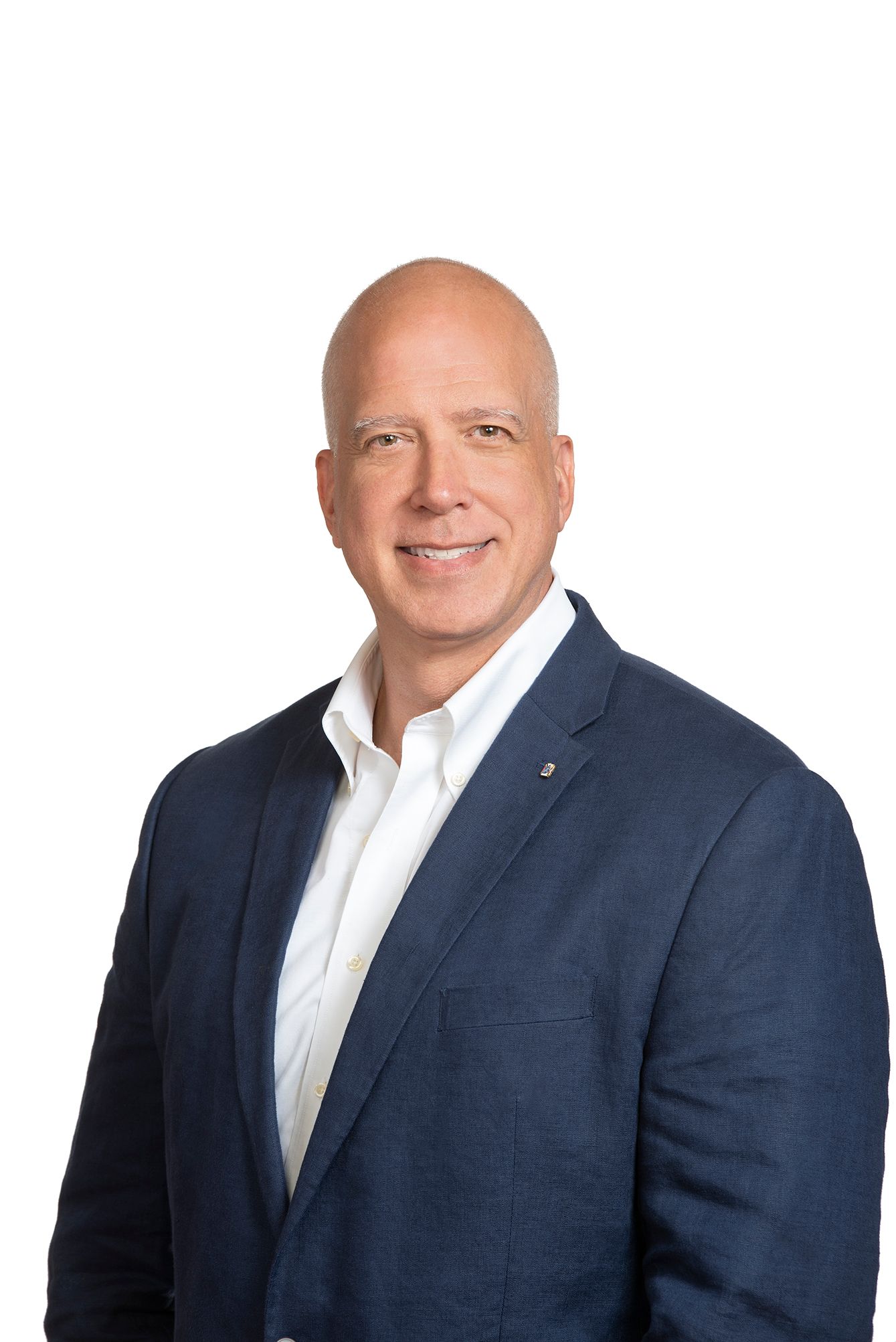 Professional headshot of a bald man in a navy blazer and white shirt smiling confidently against a white background.
