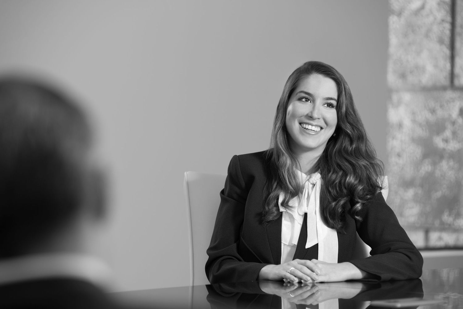Professional woman in black blazer smiling during a business meeting at a conference table, black and white photo.