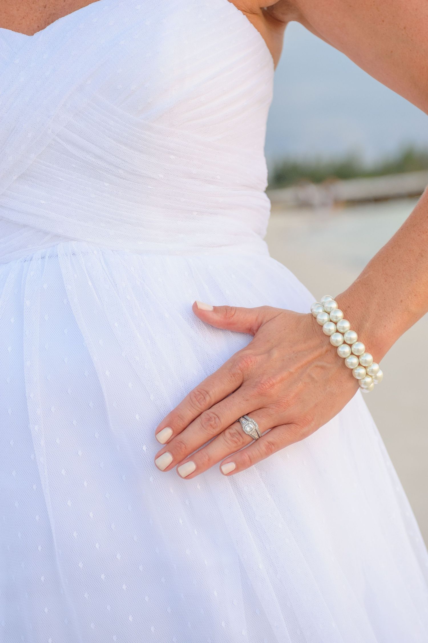 Close-up of bride's hand showing diamond engagement ring and pearl bracelet on wedding day.