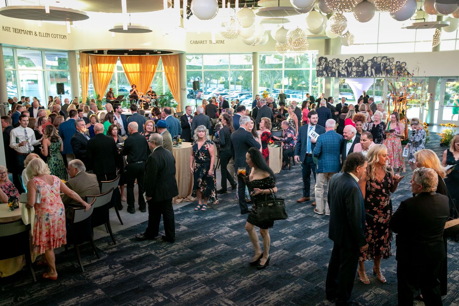 Elegant indoor gala event with well-dressed guests mingling in a spacious venue decorated with hanging ornaments.