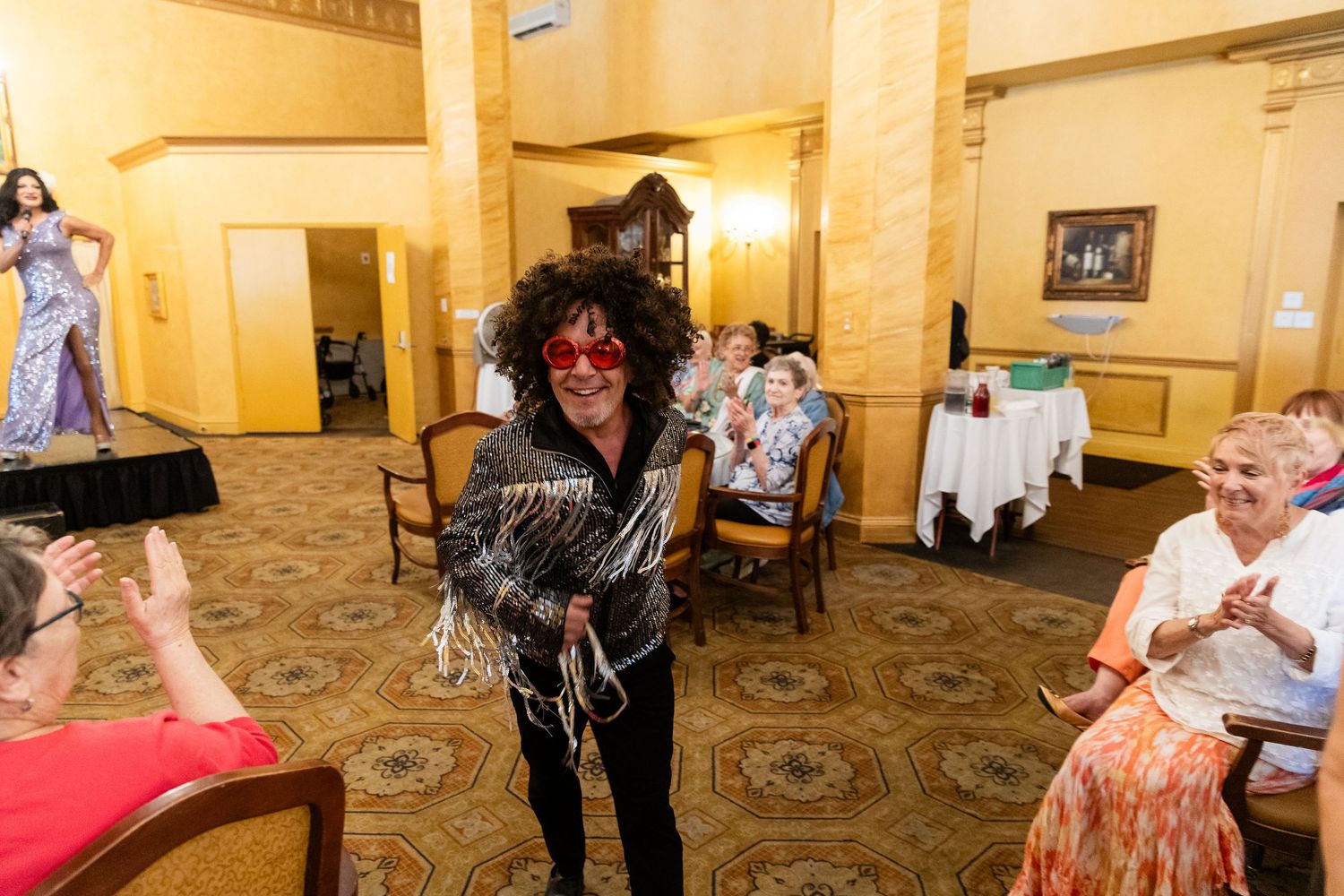 Person in festive costume with red mask and curly wig entertaining guests at an elegant indoor party event.