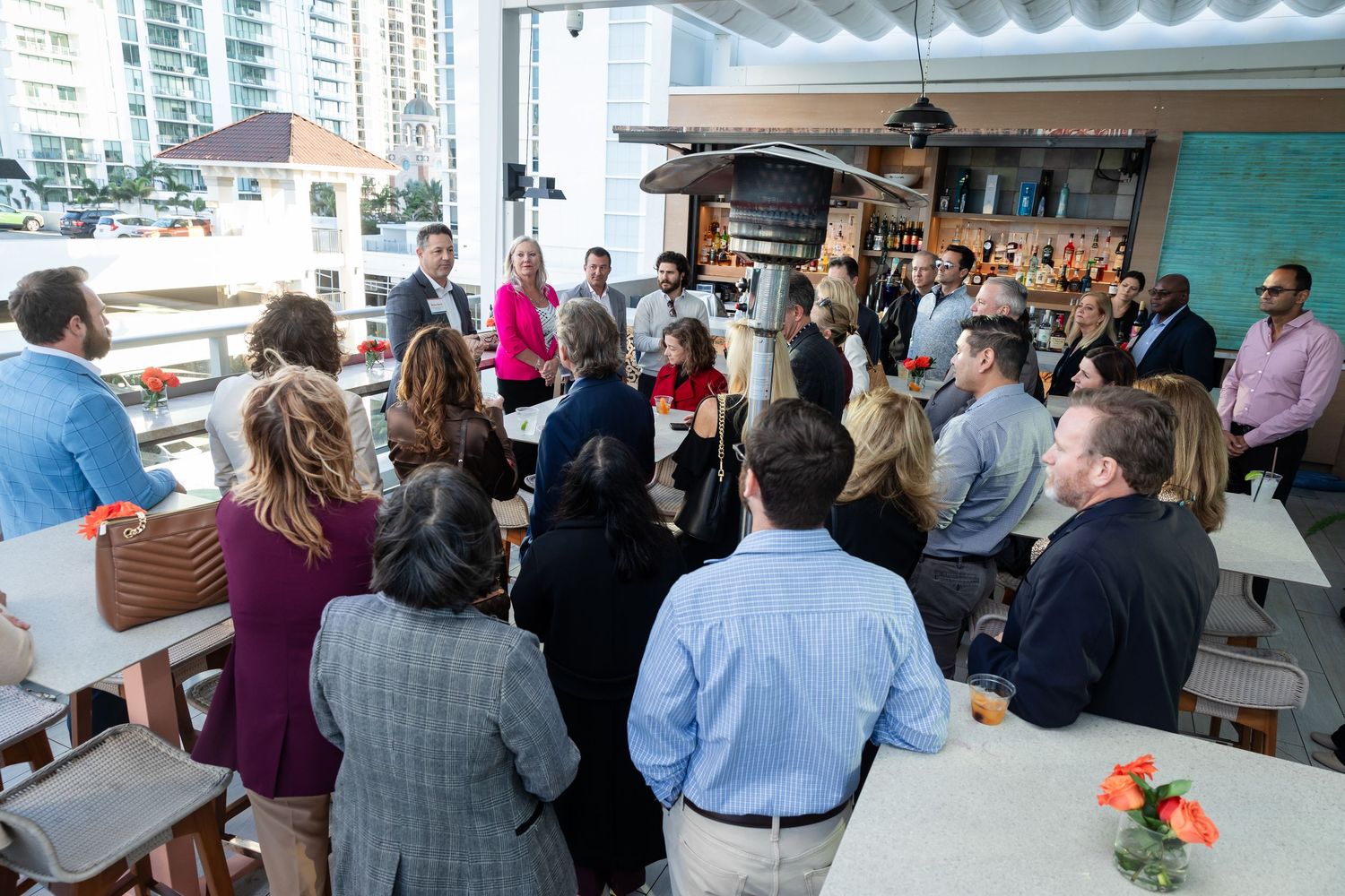 A large group of professionals gather around a speaker at an outdoor rooftop venue during a business event.
