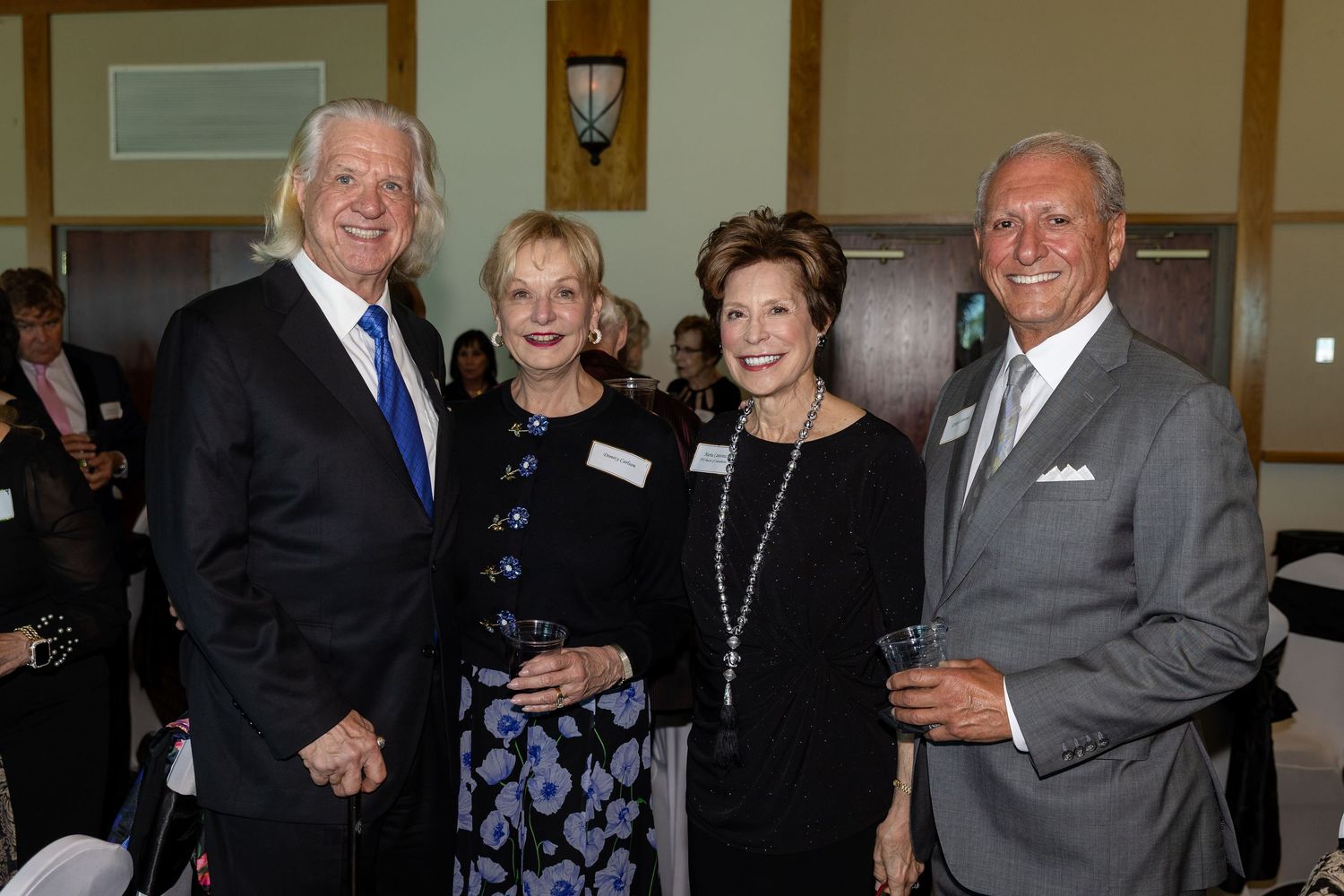 Four elegantly dressed guests smiling together at a formal networking event or gala celebration.