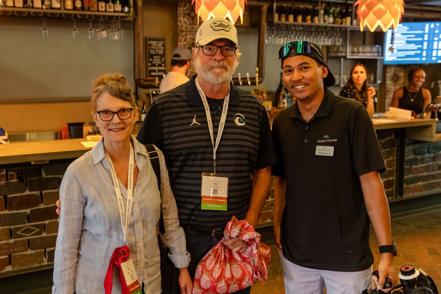 Two guests pose with a brewery staff member inside a craft beer bar.