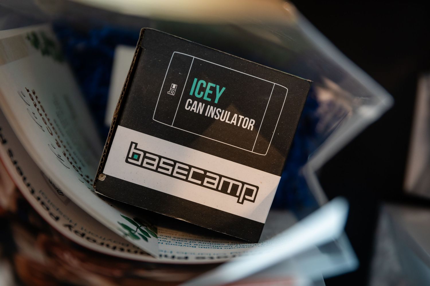 Basecamp Icey Can Insulator product box displayed among papers at an outdoor event.