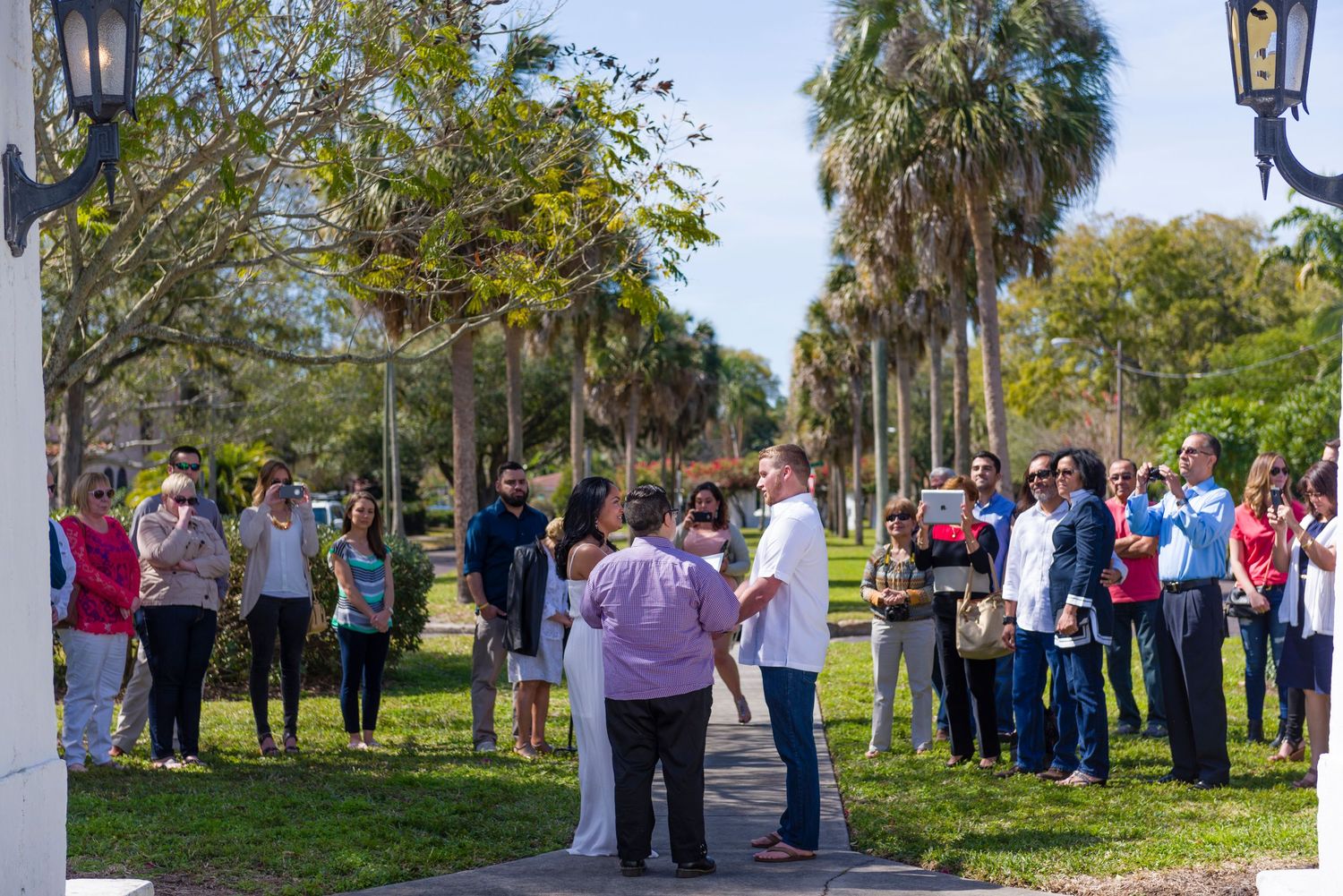 Outdoor wedding ceremony with guests gathered under palm trees on a sunny day in a tropical Florida setting.