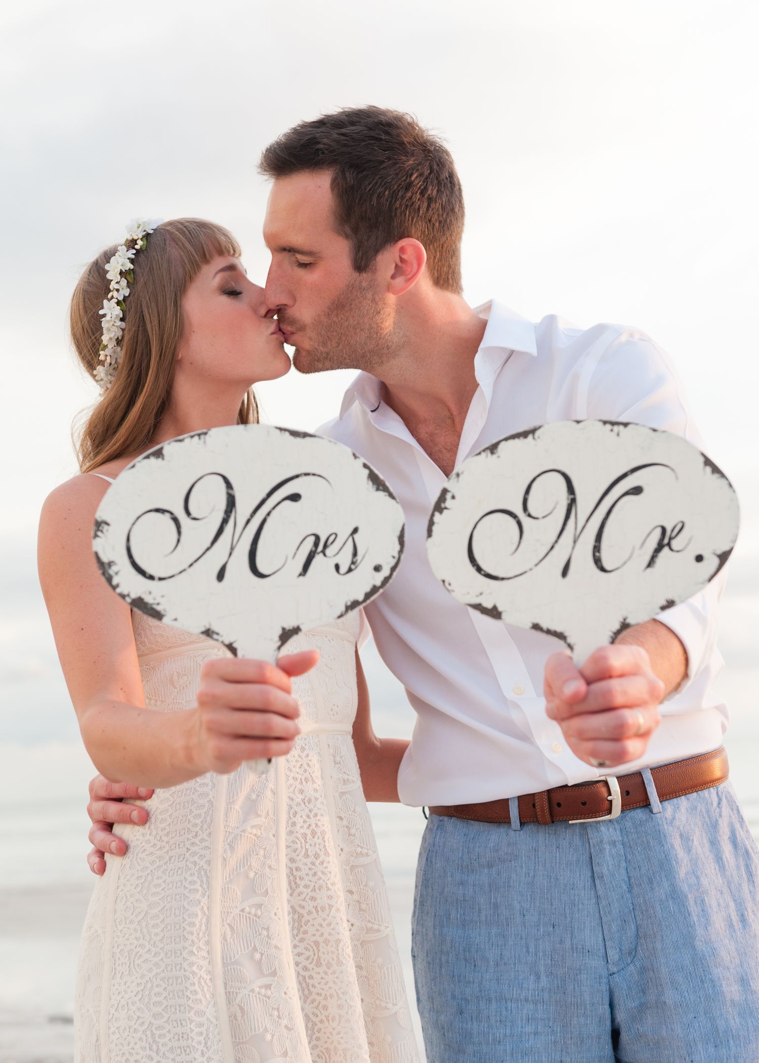 Newlyweds kissing while holding vintage Mr. and Mrs. signs at their beach wedding.