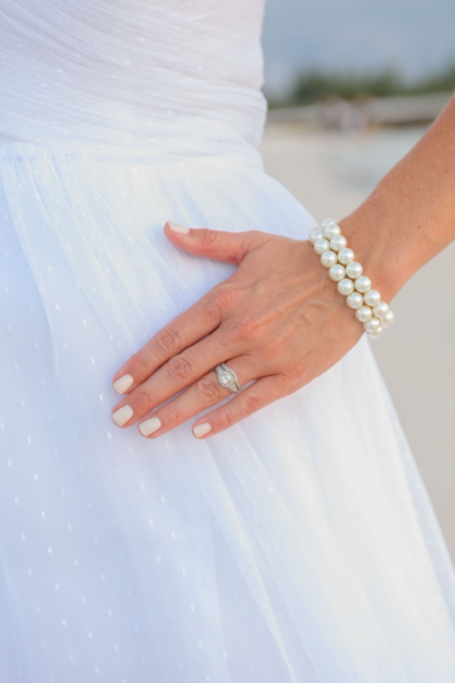Close-up of a bride's hand wearing a diamond ring and elegant pearl bracelet on her wedding day.