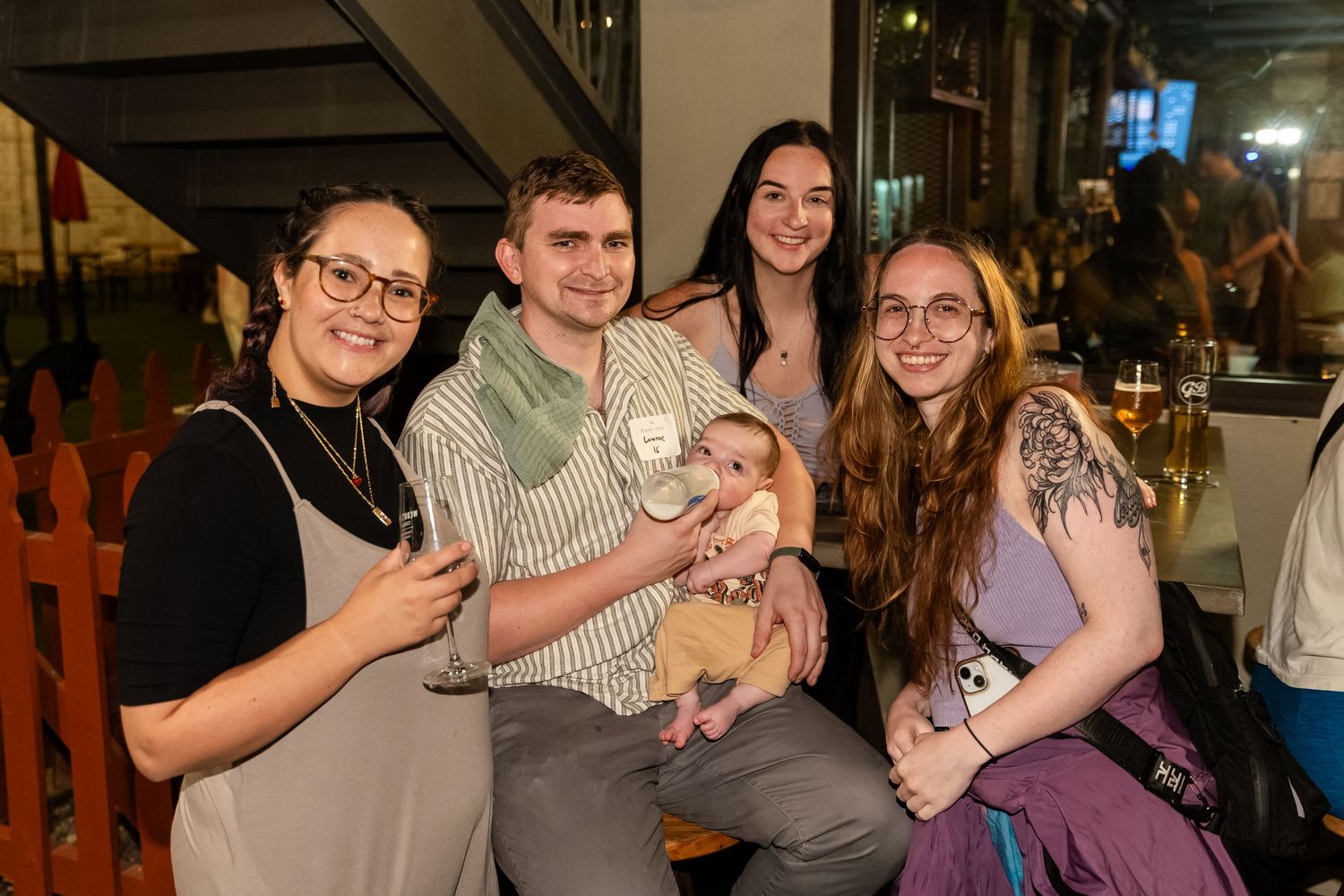 A group of five friends pose together outdoors at a casual evening social event.
