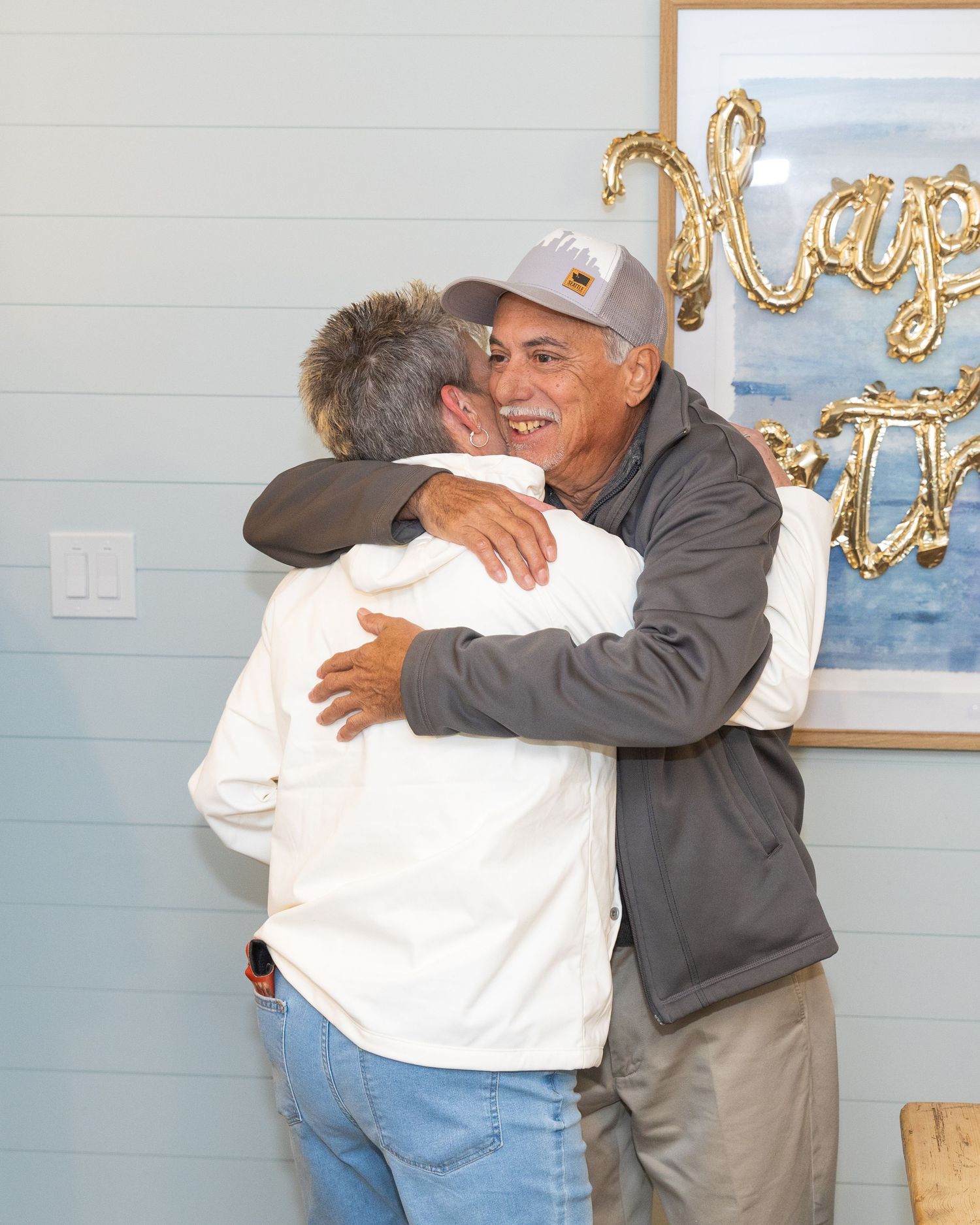 Two men sharing a warm hug at a birthday celebration indoors.