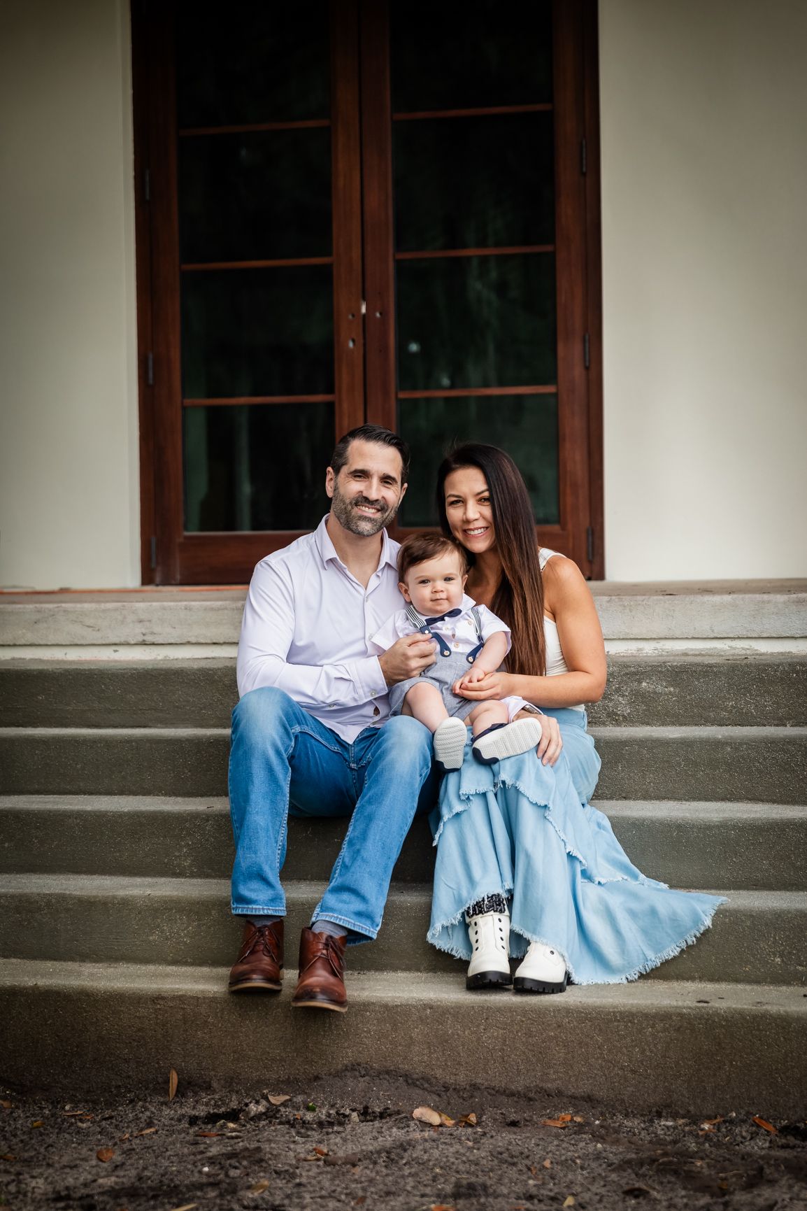 Happy family portrait with parents and baby sitting on stone steps in front of a classic building door.