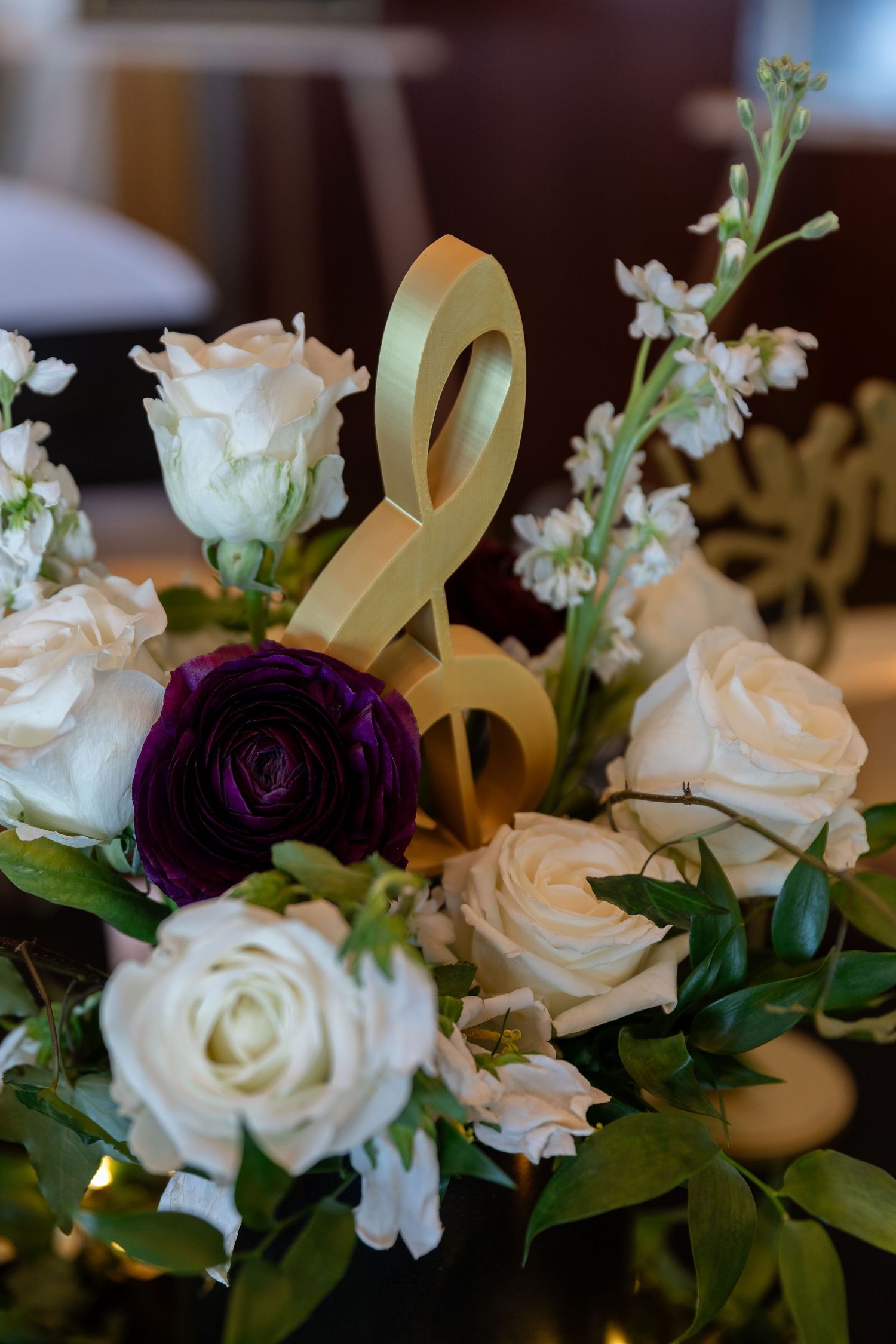 Gold treble clef decoration among white roses and purple ranunculus in an elegant floral centerpiece arrangement.