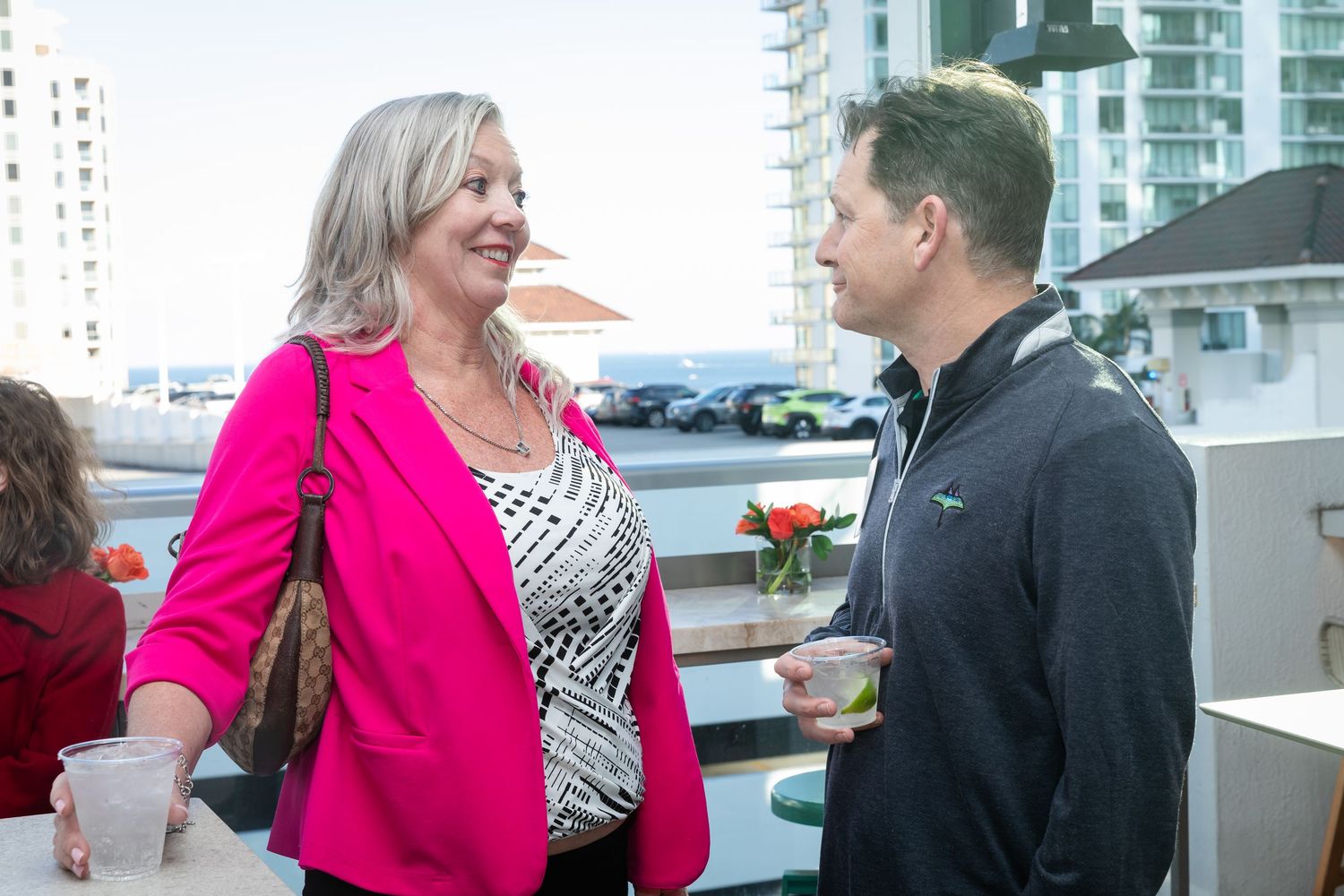 Two professionals networking at an outdoor rooftop event, woman in pink blazer conversing with man holding a drink.