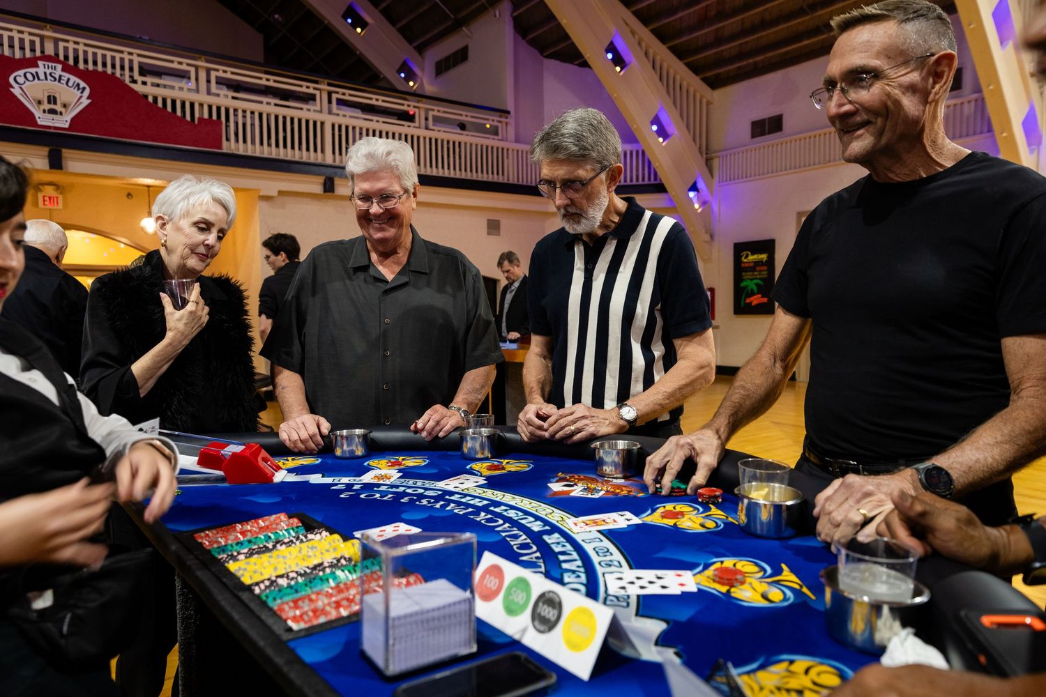 Four adults laughing and playing a casino card game at a colorful table during an indoor event.