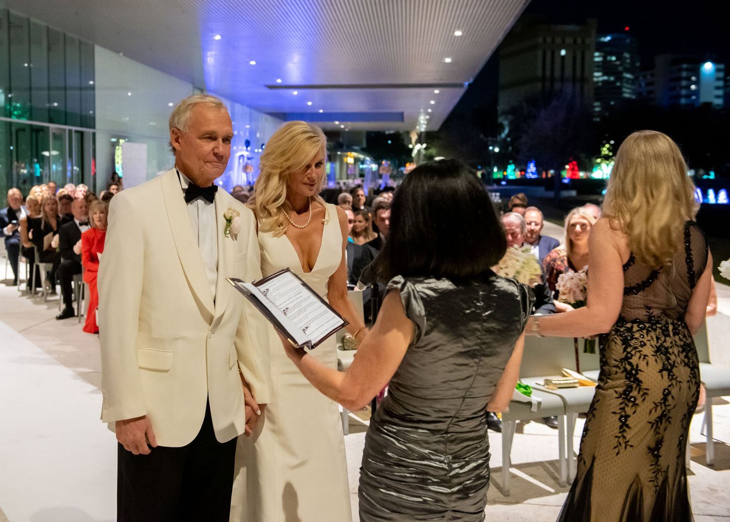 Elegantly dressed guests at a formal gala event, with a woman presenting an award to a couple in evening wear.