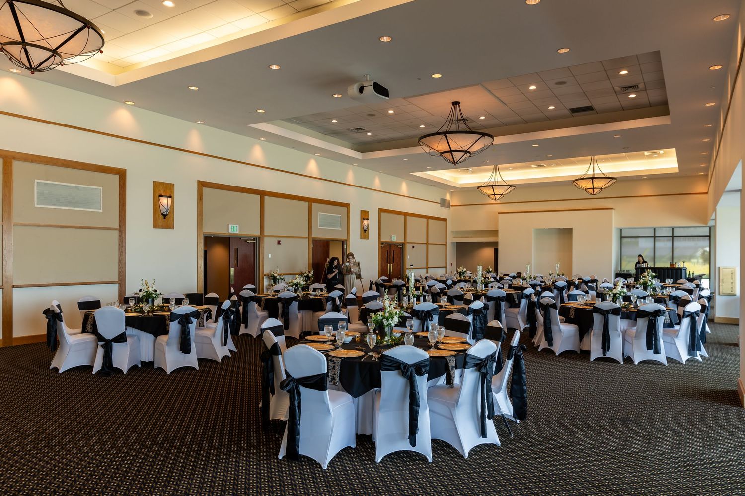 Elegant banquet hall with round tables draped in white linens, black chair sashes, and floral centerpieces for a formal event.