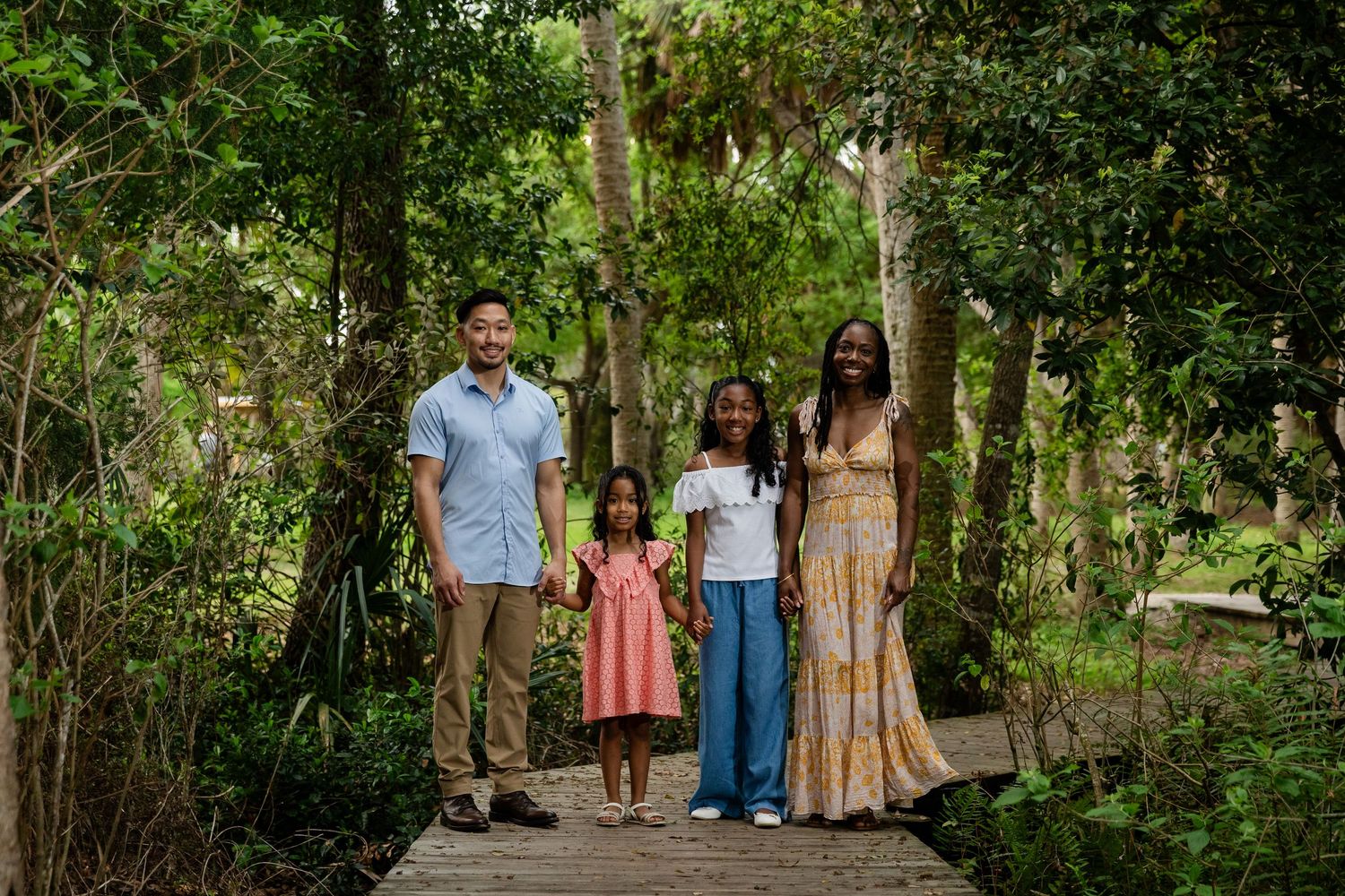 Family of four smiling together on a wooden bridge surrounded by tropical greenery.