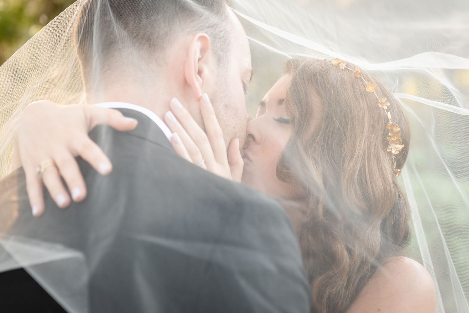 Bride and groom sharing romantic kiss under flowing white veil on wedding day.