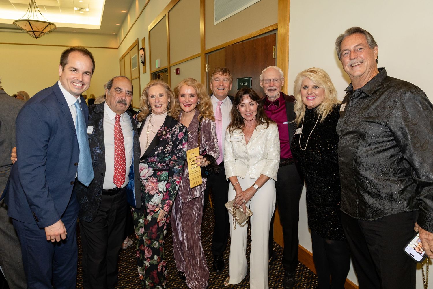 Group of elegantly dressed adults smiling together at a formal event or gala celebration indoors.