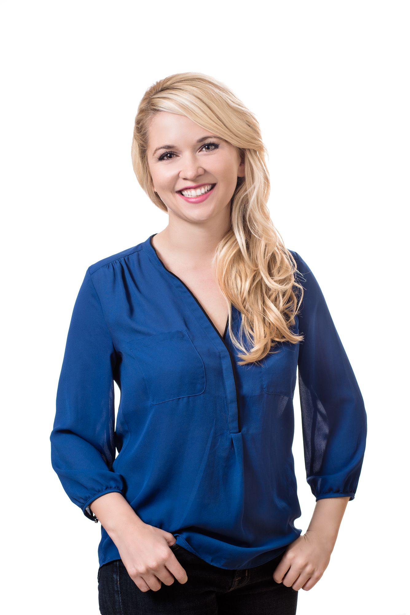 Smiling blonde woman in a blue V-neck blouse posing against a white background.