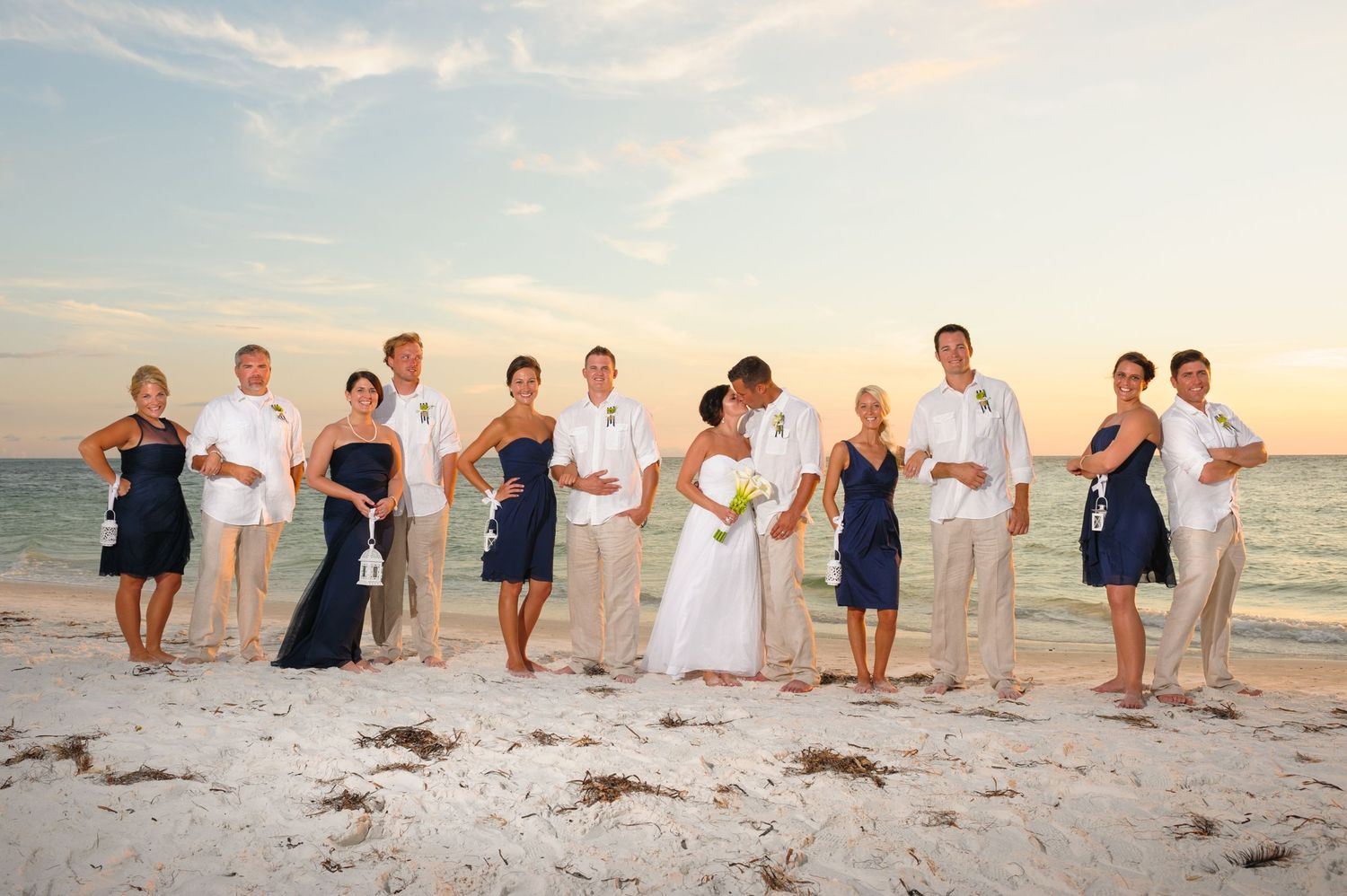 Wedding party posing on a sunny beach, bridesmaids in navy blue dresses and groomsmen in khaki.