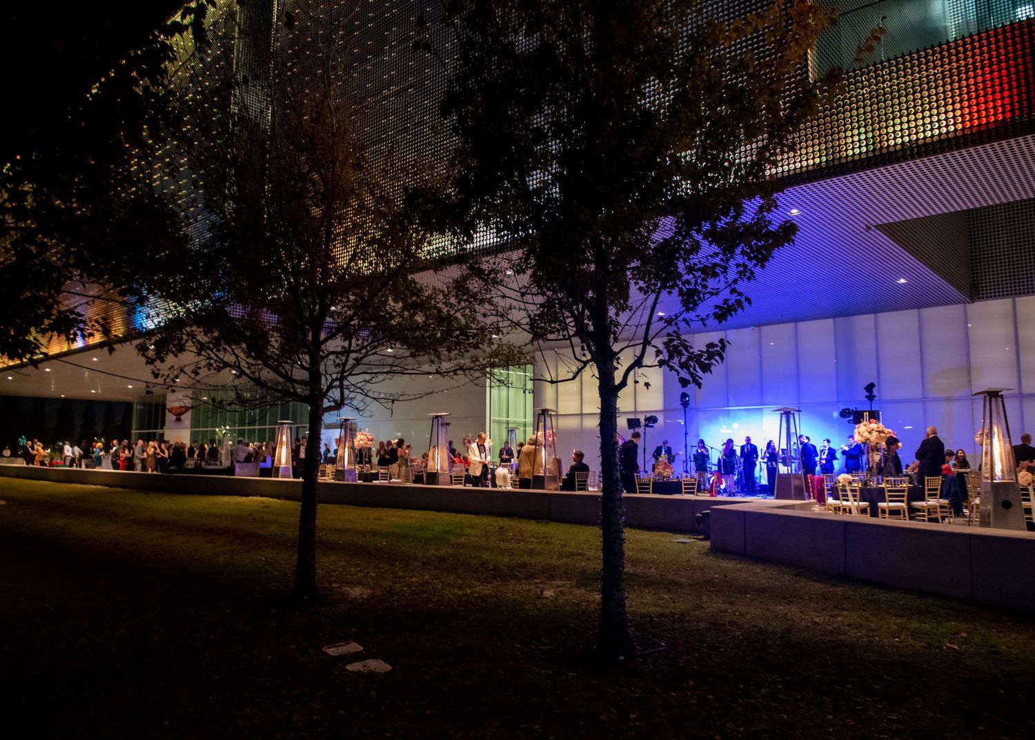 Elegant outdoor wedding reception at night with blue-lit venue exterior and guests mingling on terrace at Tampa museum of fine art.