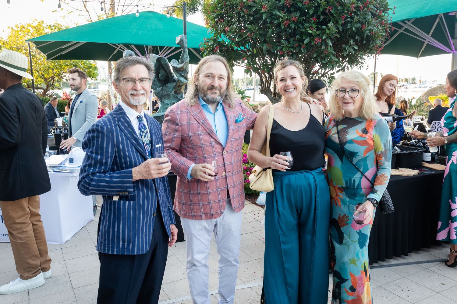 Four elegantly dressed guests posing together at an outdoor social event with green umbrellas.