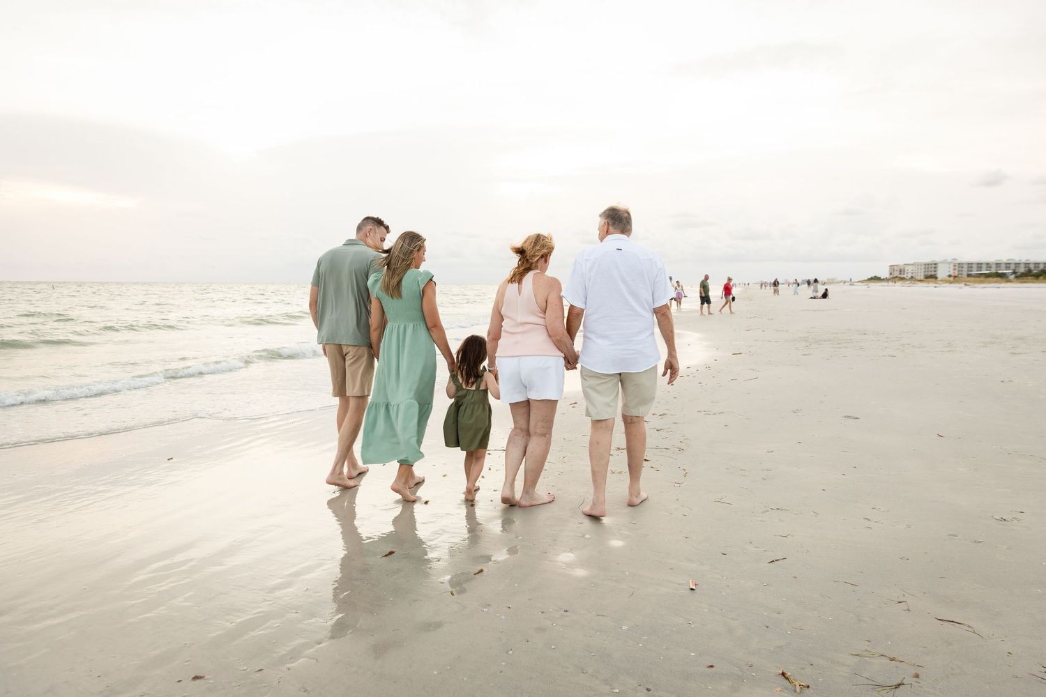 Family walking along shoreline at sunset, dressed in coordinating green and white beach outfits.