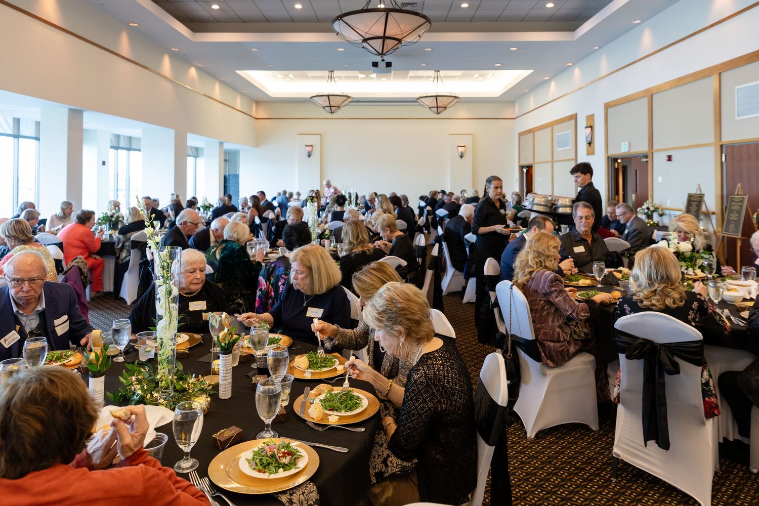 Large group of guests dining at elegantly decorated tables during formal banquet event.