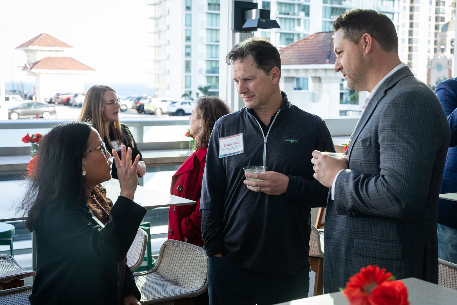 Professionals networking at an outdoor rooftop event with city buildings in the background.