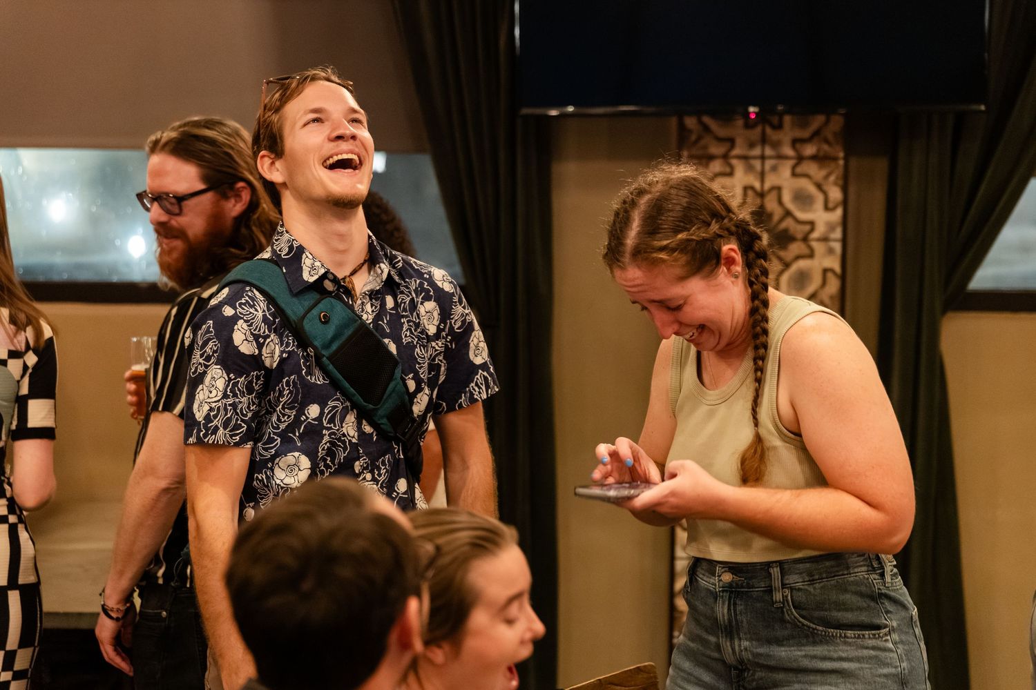 Young adults laughing and enjoying themselves at a casual indoor social gathering.