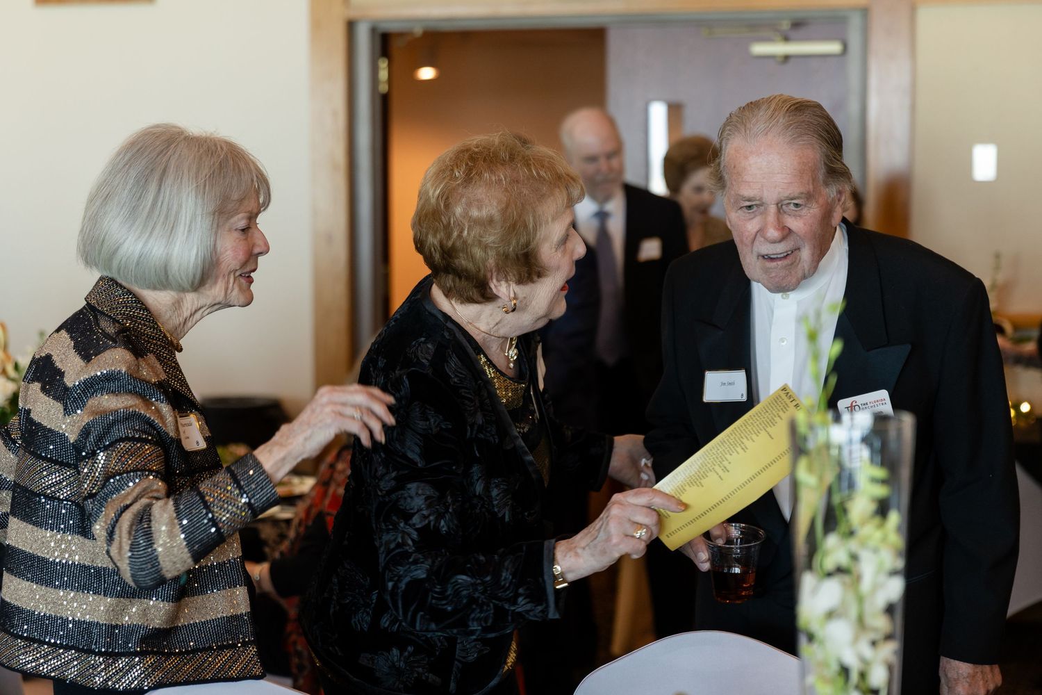 Elderly group of seniors socializing at a formal event, exchanging papers and smiling in an elegant venue.