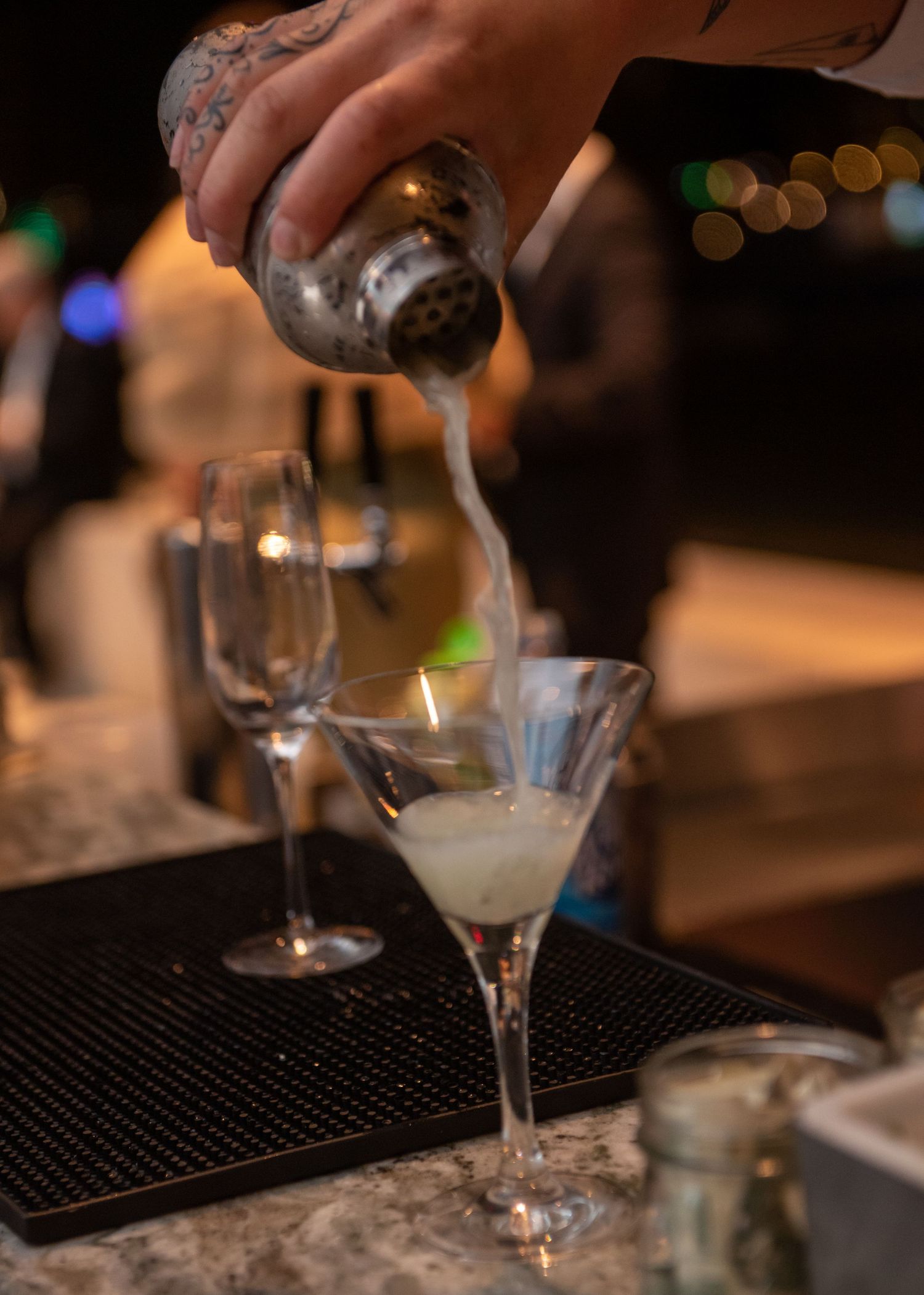 Bartender pouring a chilled martini cocktail into a glass at a wedding reception bar.