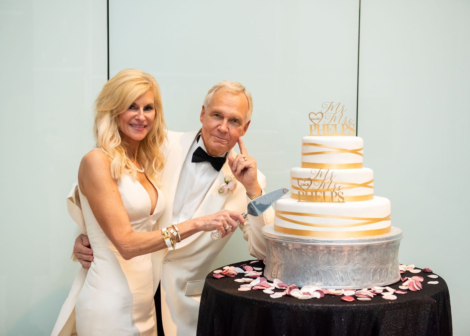 Couple cuts a tiered white and gold anniversary celebration cake at a formal event.