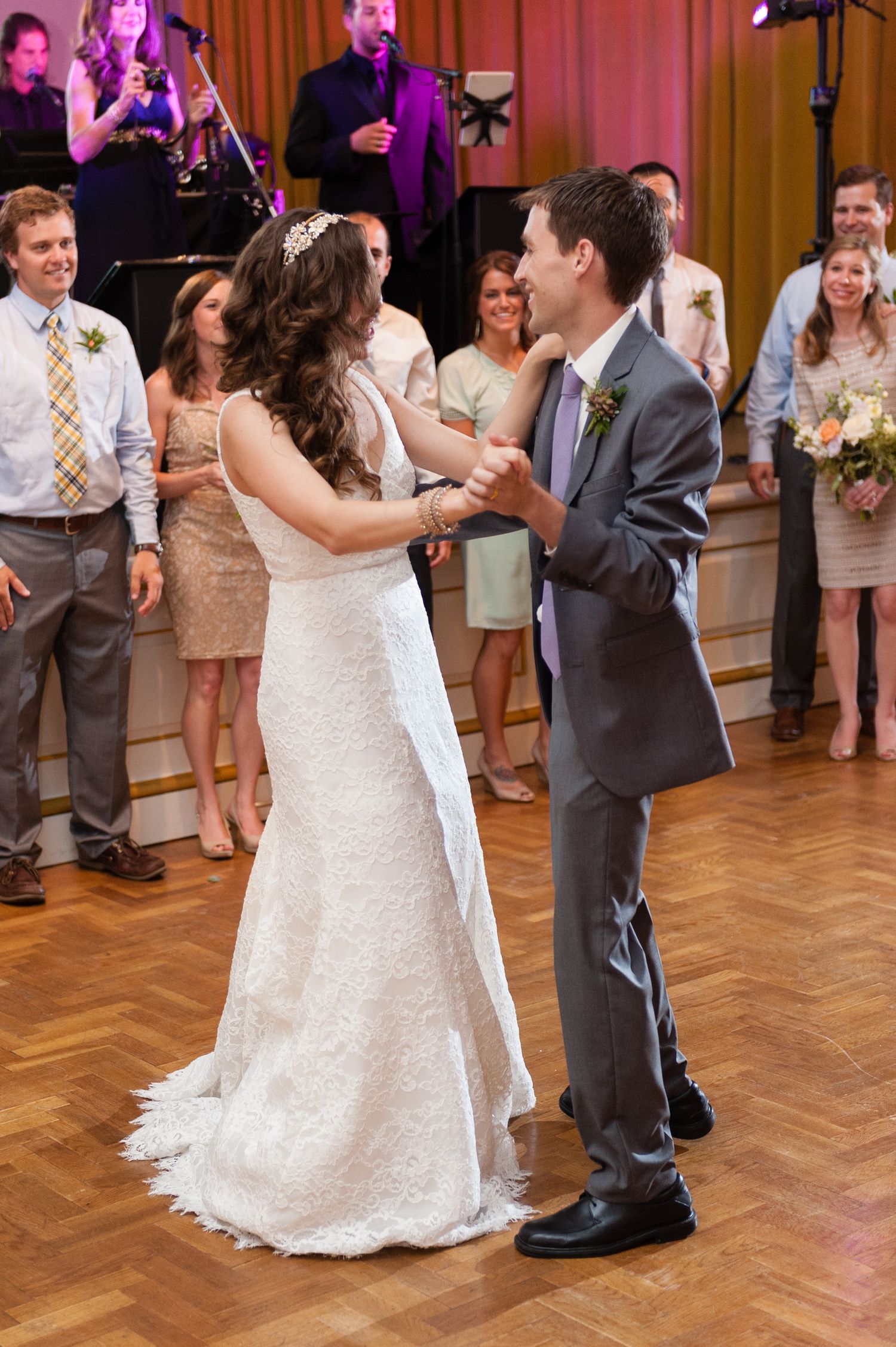Bride and groom share their first dance at wedding reception with guests watching in background.