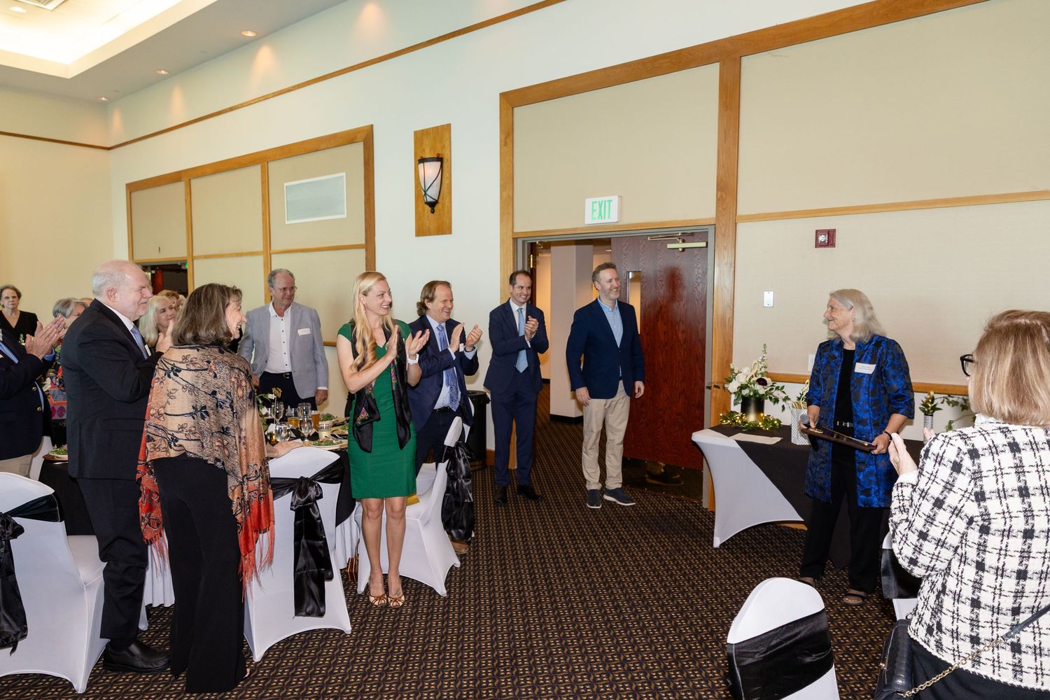 Guests mingle and applaud at an elegant indoor networking event in a well-lit banquet room.