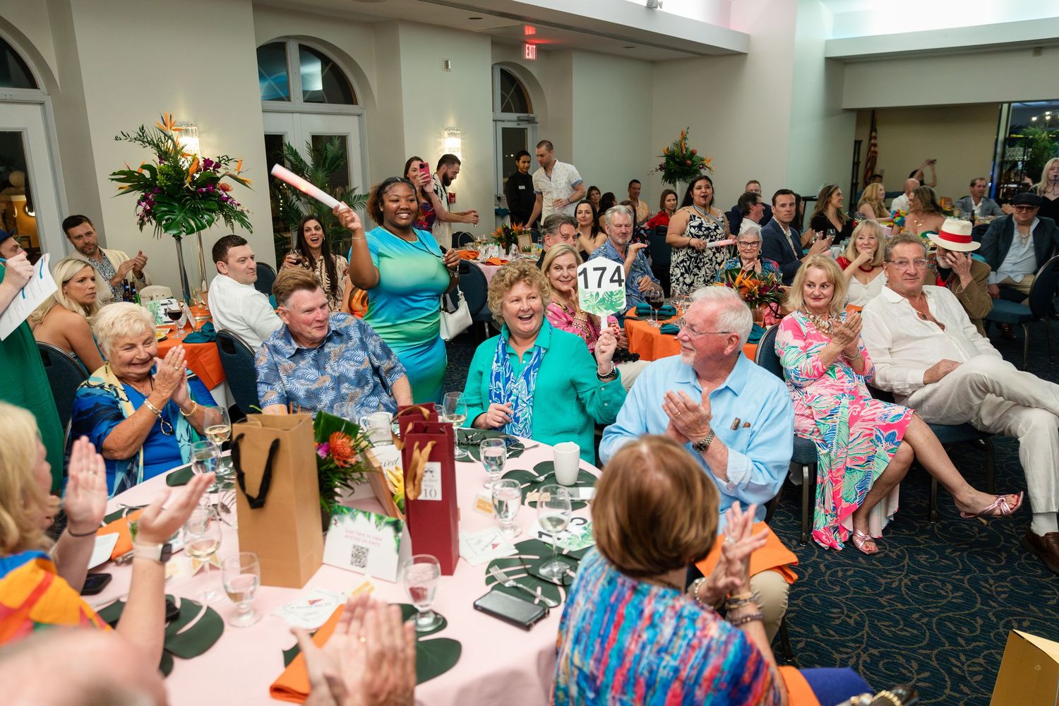 Guests clapping and celebrating at an elegant indoor banquet event with colorful attire and festive decorations.