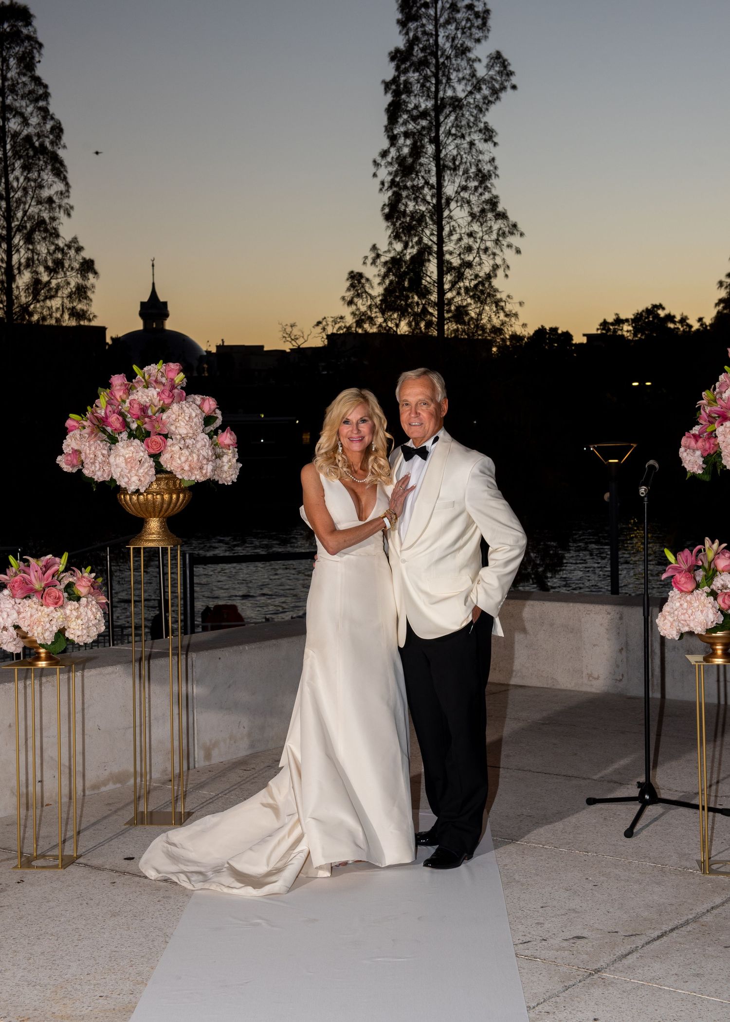Elegant couple poses at outdoor wedding ceremony at dusk with pink floral arrangements and waterfront backdrop at Tampa museum of fine art.
