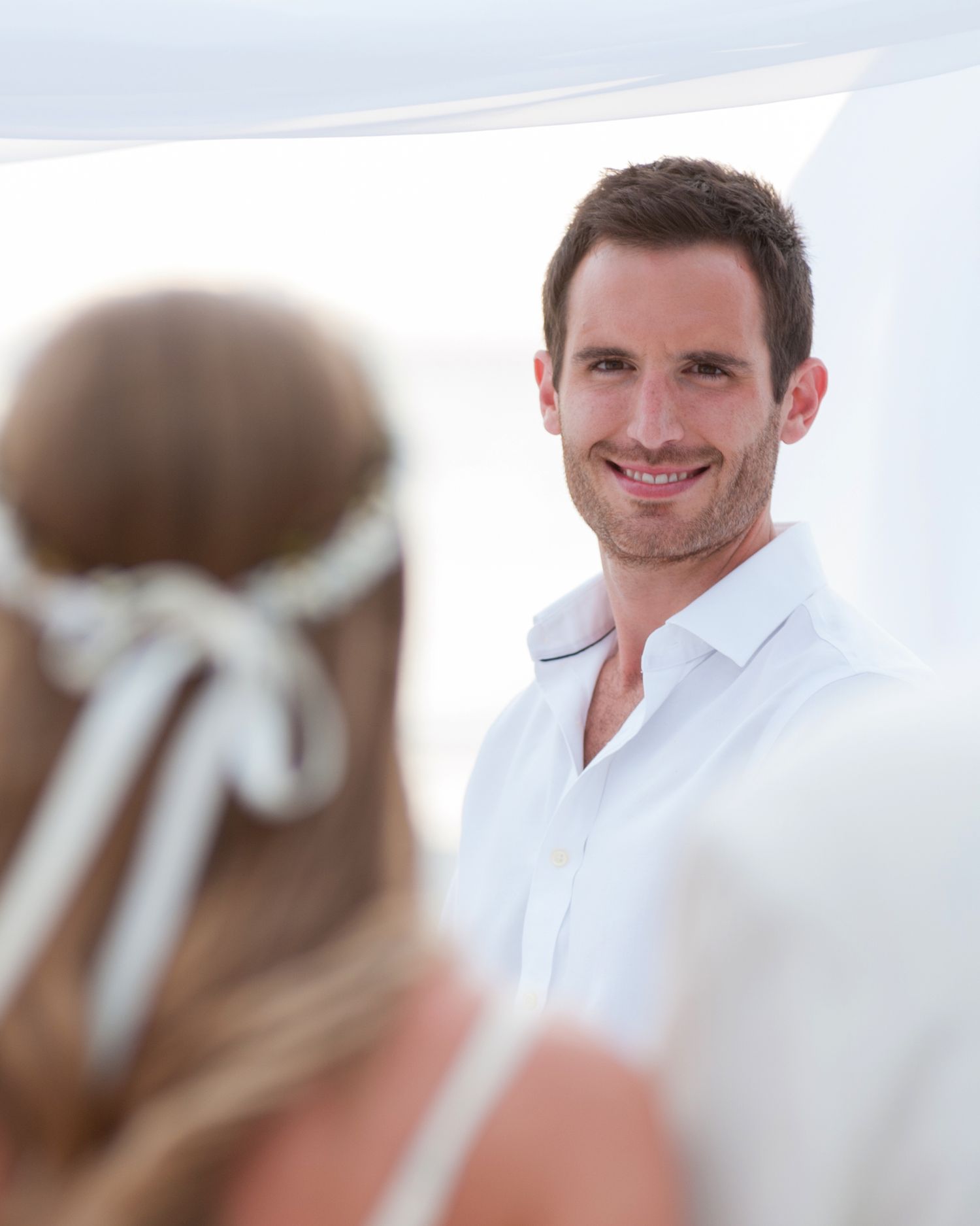 Handsome groom in white shirt smiles warmly at bride during intimate beach wedding ceremony on Treasure Island, Florida.