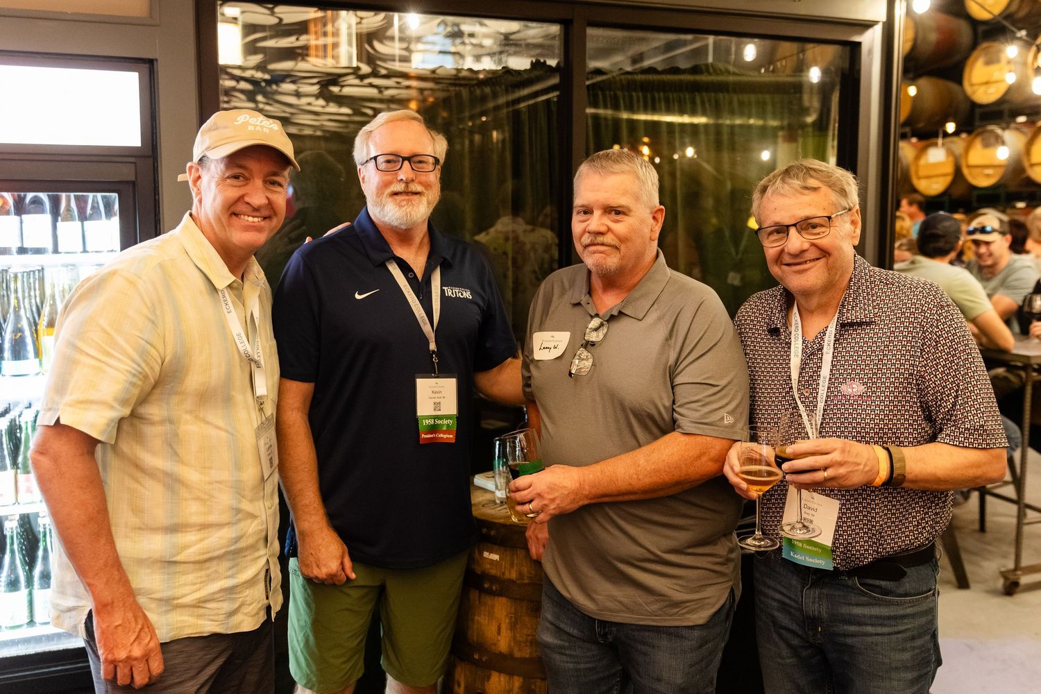 Four men smiling and holding wine glasses at a brewery networking event.